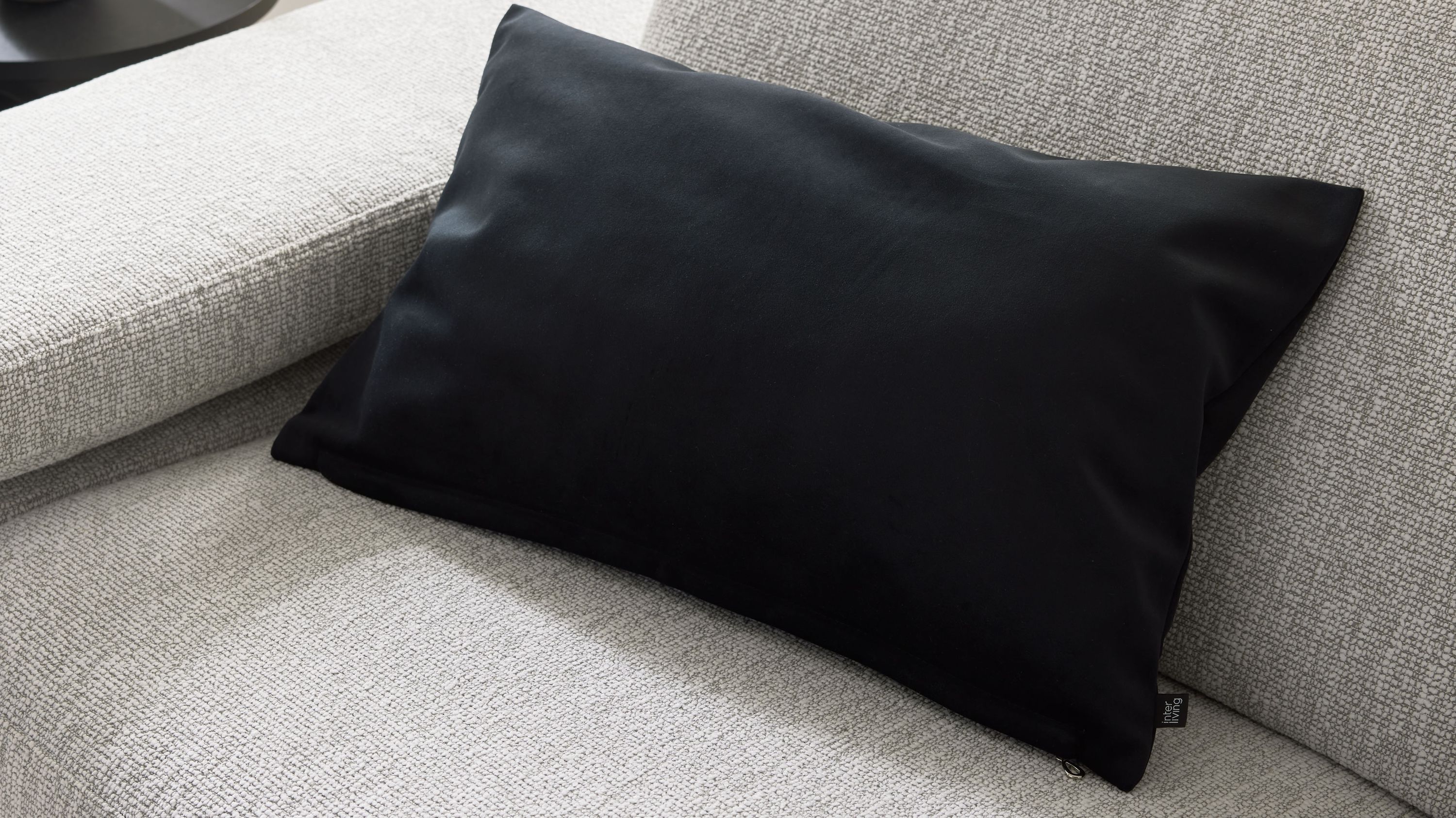 Rechteckige schwarze Kissenhülle auf hellgrauem Sofa