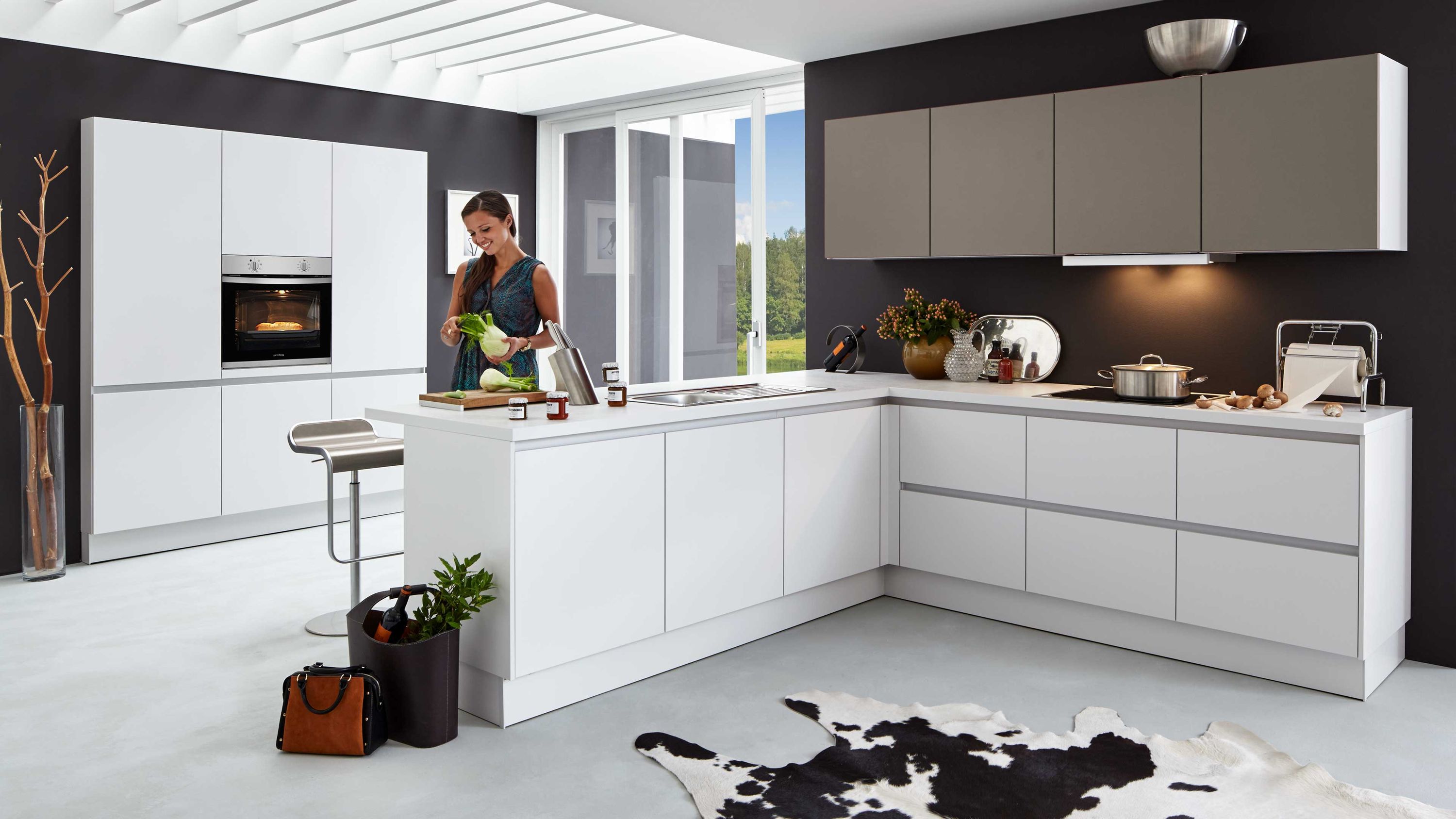 Moderne weiße L-Küche mit grauen Hängeschränken. Weiße L-Küche mit grauen Hängeschränken Kochinsel Einbauofen und dunkler Rückwand im modernen Design.