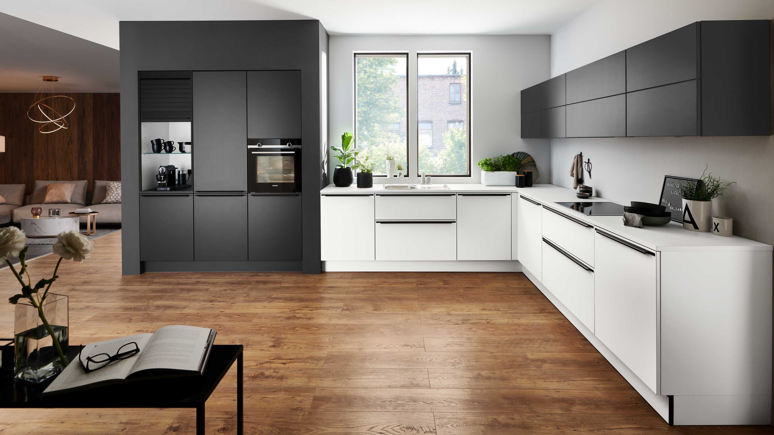 Küche mit Kontrastfronten und Blick ins gemütliche Wohnzimmer Küche mit weißen und grauen Schränken Holzboden Fensterlicht Tisch mit Buch und Durchgang zum Wohnbereich