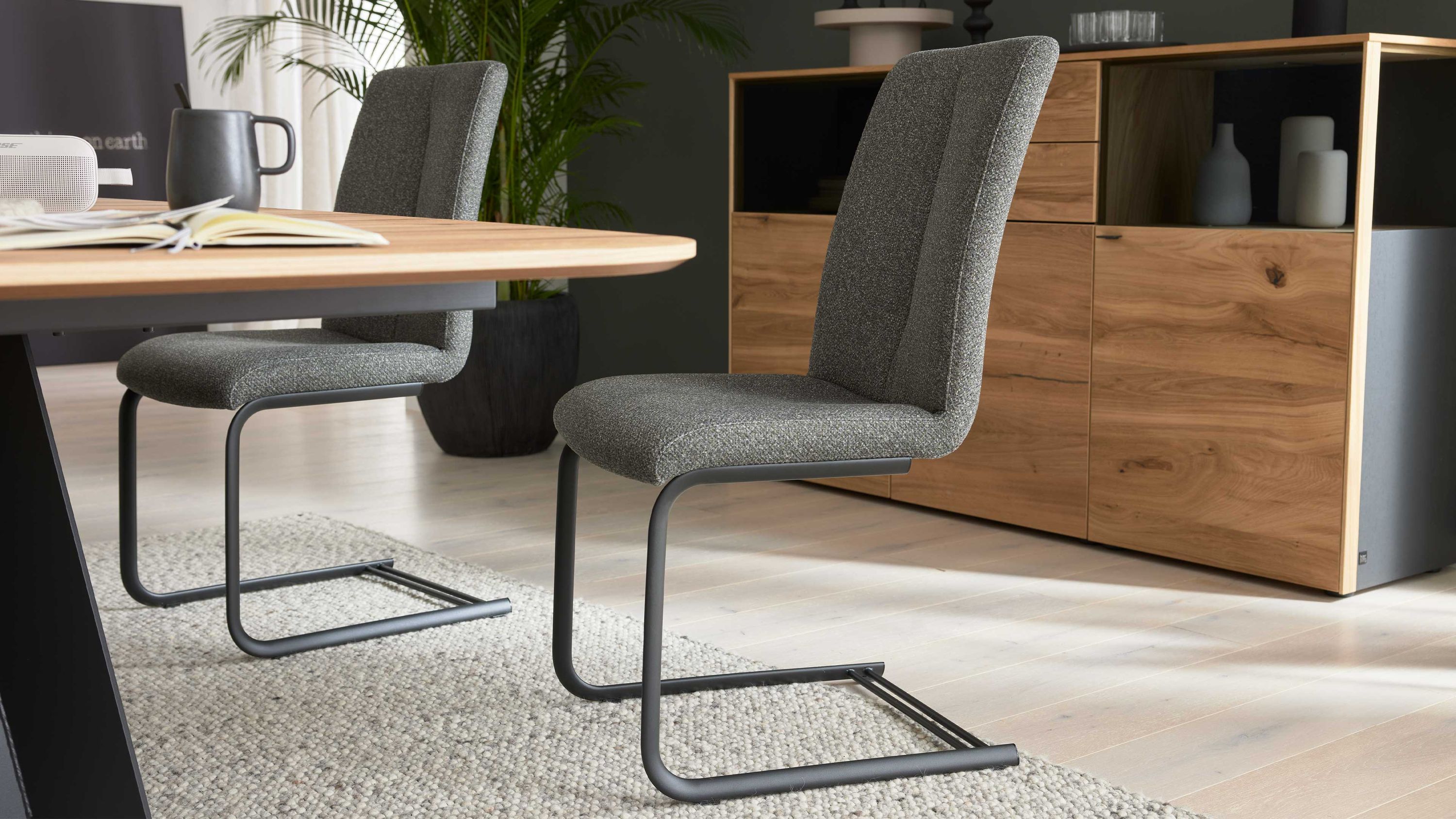 Zwei anthrazitfarbene Schwingstühle mit grauem Stoffbezug an einem Holztisch in einem Esszimmer mit Sideboard