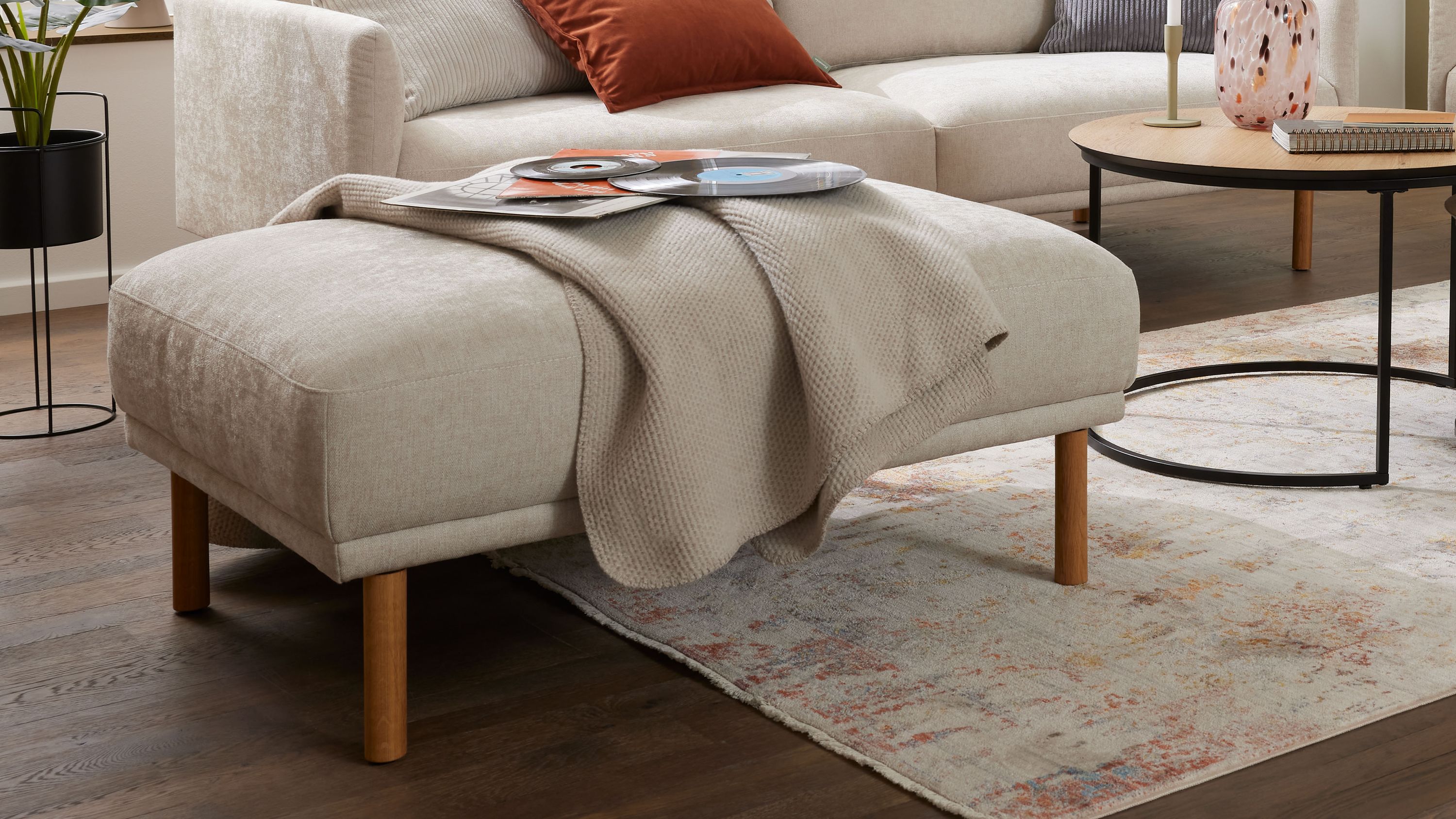 XXL-Polsterhocker mit naturfarbenem Bezug und Holzfüßen Großer rechteckiger Polsterhocker mit naturfarbenem Bezug und vier Holzfüßen in einem Wohnzimmer