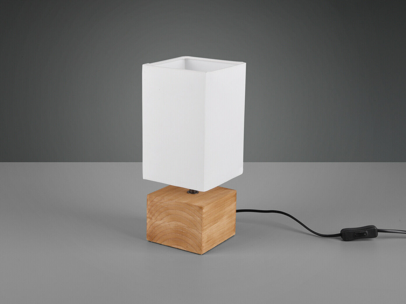 Tischlampe mit Holzfuß und weißem rechteckigem Schirm auf grauer Fläche, Stromkabel sichtbar