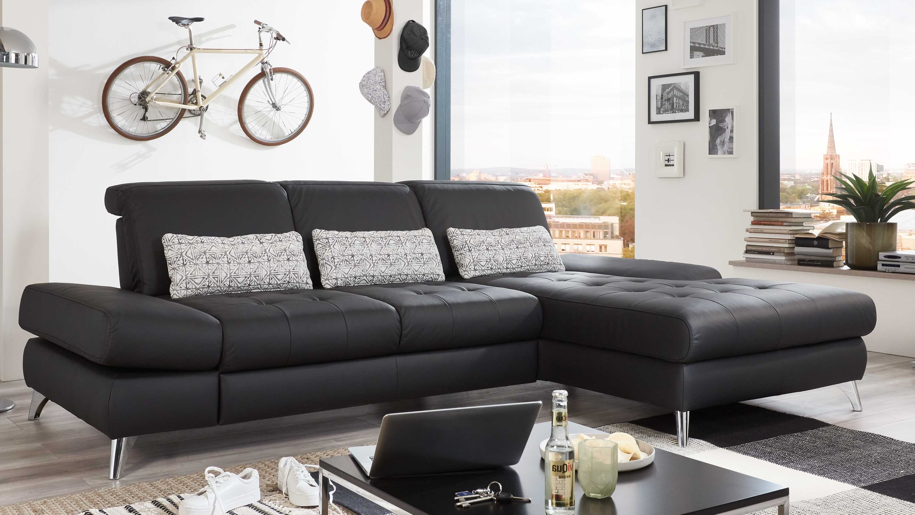 Schwarzes Ecksofa mit Chromfüßen Ecksofa mit schwarzer Polsterung und Chromfüßen drei gemusterte Kissen modernes Wohnzimmer mit Fenster