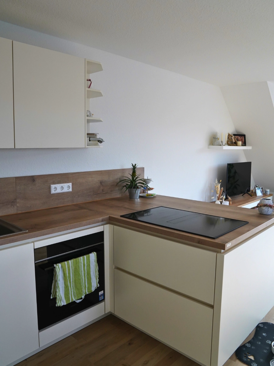 Helle L-Küche mit Kochinsel, Holzarbeitsplatte, weißen Fronten, Induktionskochfeld und Dekoration auf Parkettboden.