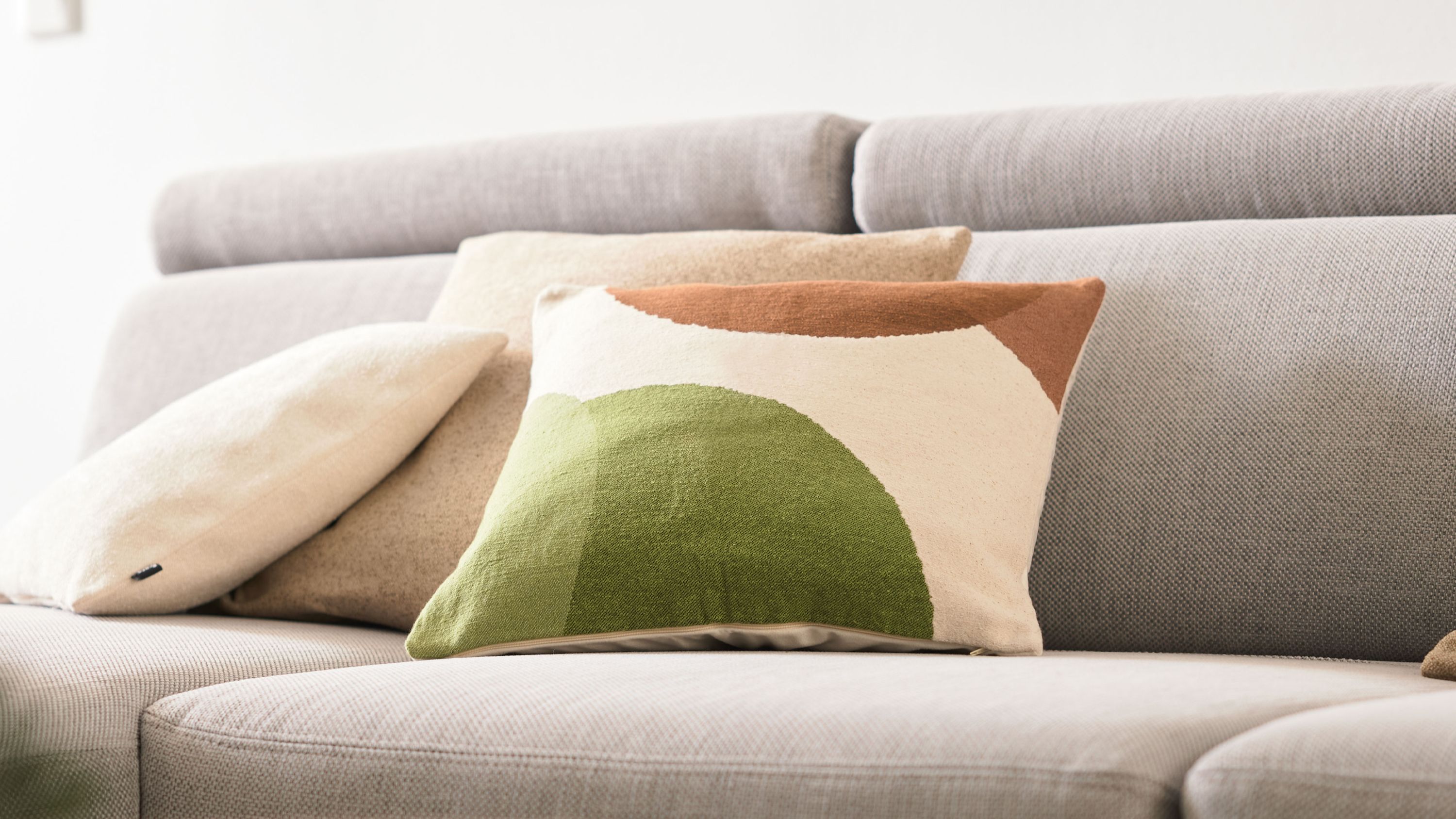 Kissen mit grafischem Muster auf Sofa Rechteckiges Kissen mit grünem und braunem grafischem Muster auf hellgrauem Sofa