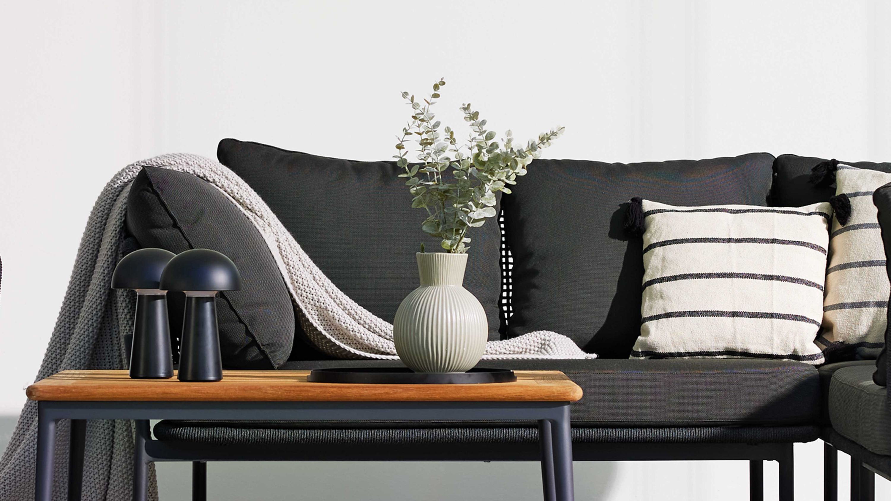 Linkes Gartensofa mit grauem Kordelgeflecht dunkelgrauen Polstern und zwei gestreiften Kissen