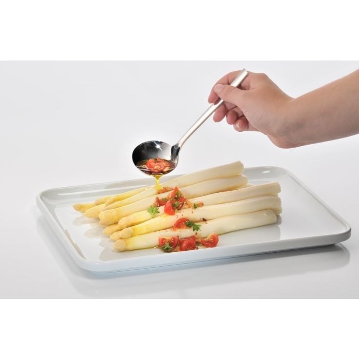 Hand träufelt mit silbernem Saucenlöffel Tomatensauce über weißen Spargel auf rechteckigem weißen Teller