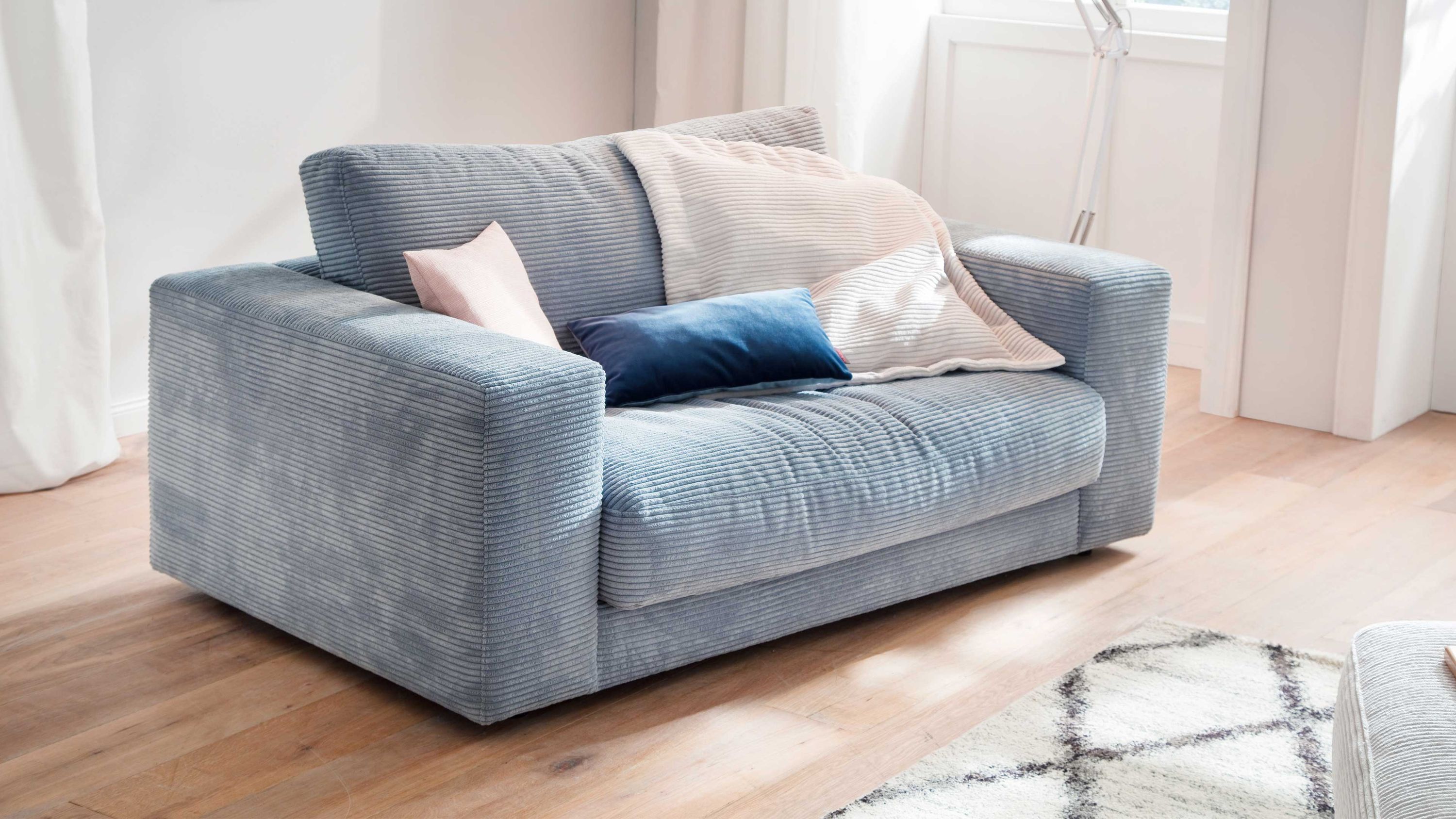 Zweisitziges Sofa mit hellblauem Cordbezug und breiten Armlehnen in einem hellen Raum