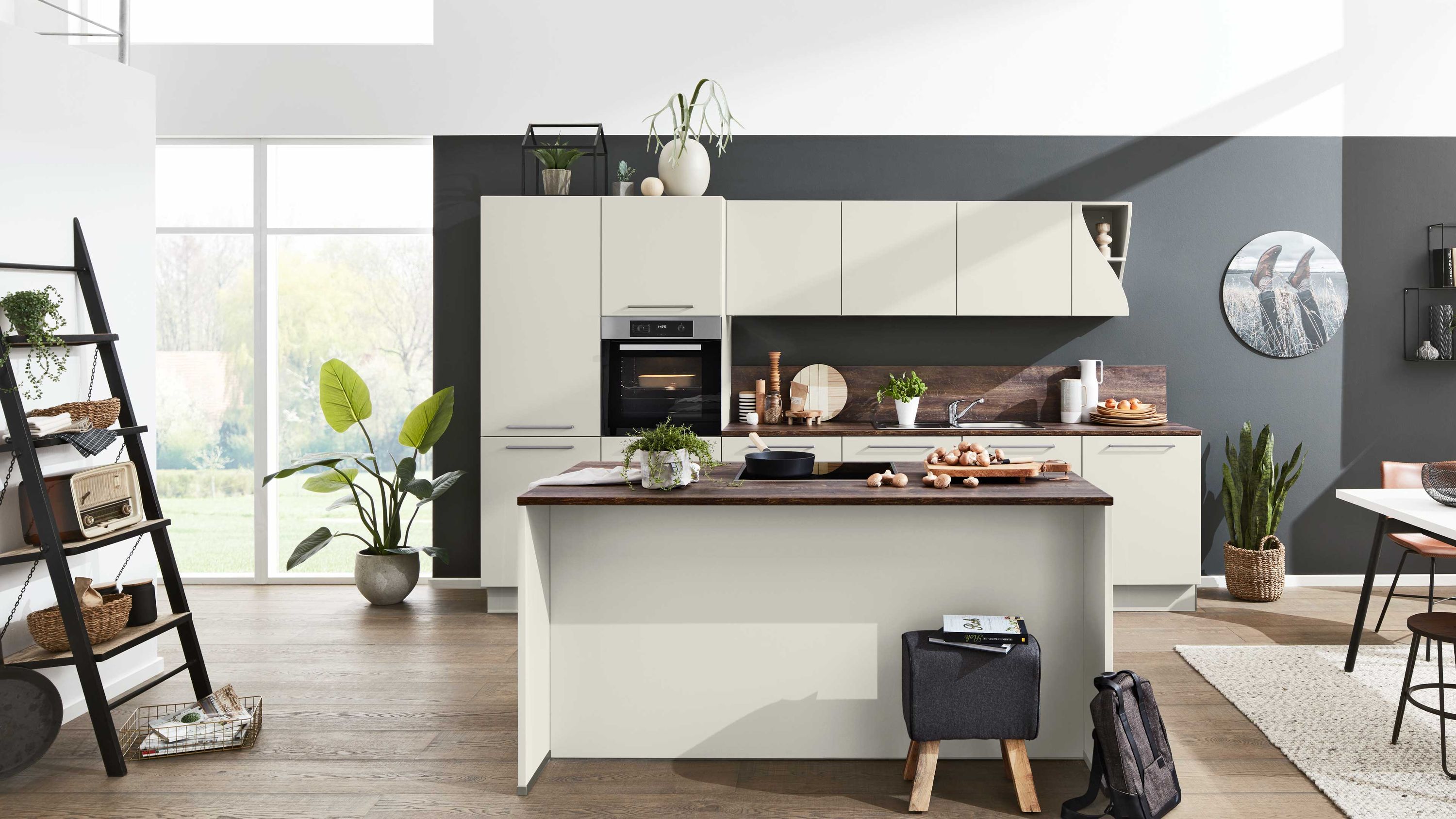 Helle Inselküche in Creme mit Holzarbeitsplatte Hängeschränken Einbauofen und dunkler Akzentwand.