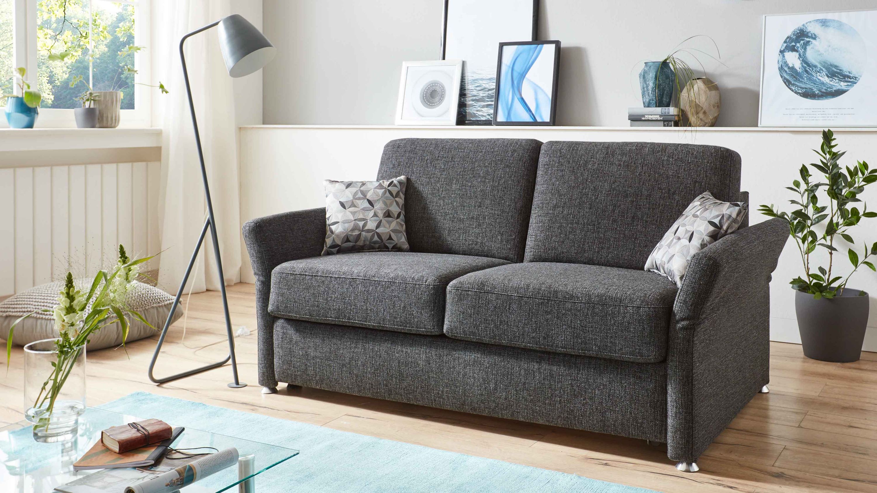 Anthrazitfarbenes Schlafsofa mit zwei Sitzkissen zwei gemusterten Kissen und Chromfüßen in modernem Wohnzimmer
