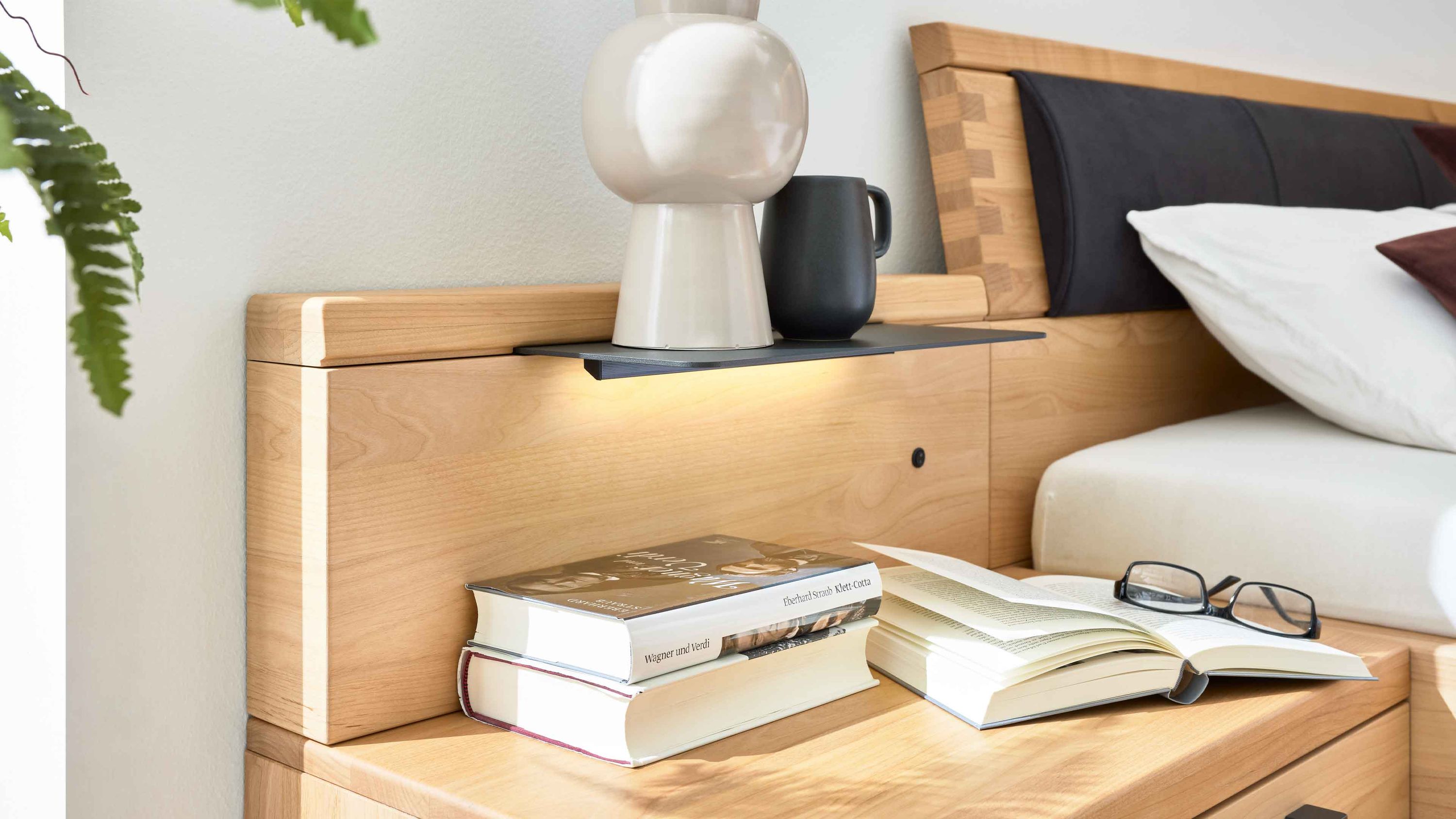 Zweiteiliges Paneelaufsatz-Set aus hellem Holz mit integrierter Beleuchtung und Ablagefläche neben einem Bett