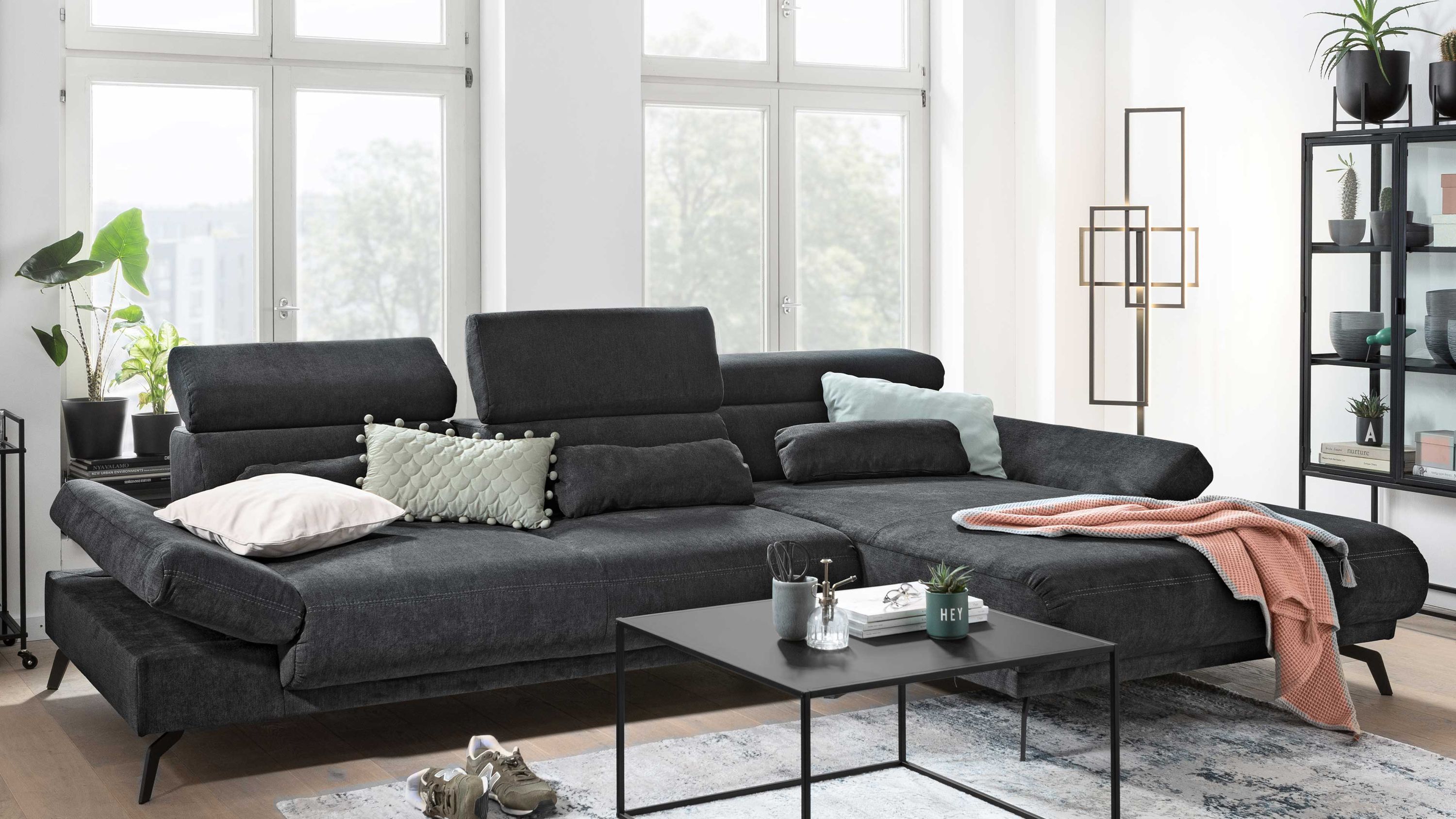 Dunkelgraues Ecksofa mit verstellbaren Armlehnen und Rückenlehnen dekoriert mit Kissen und Decke