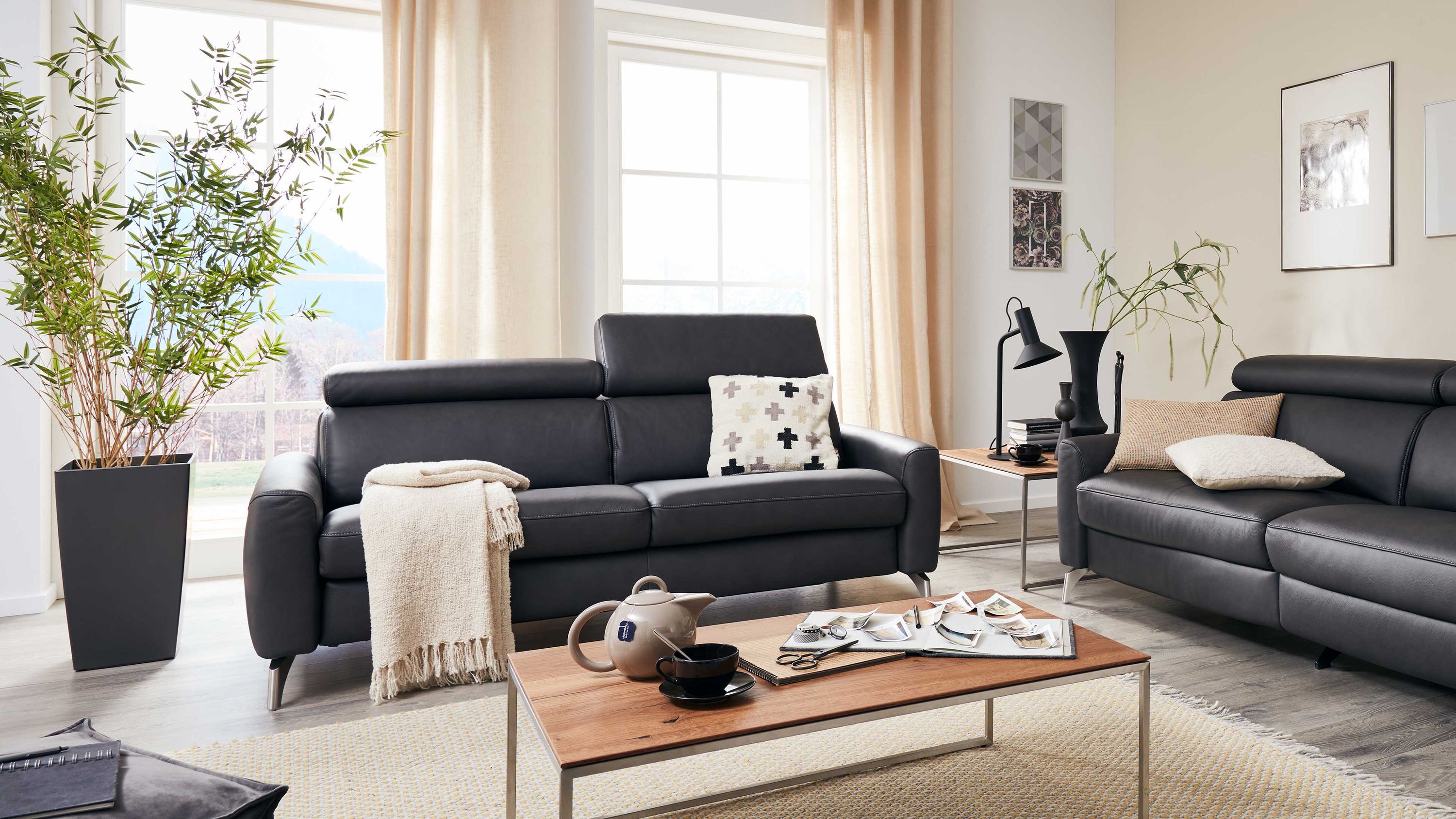 Zweisitziges Sofa in dunkler Farbe mit verstellbaren Kopfstützen und Kissen in einem hellen Wohnzimmer