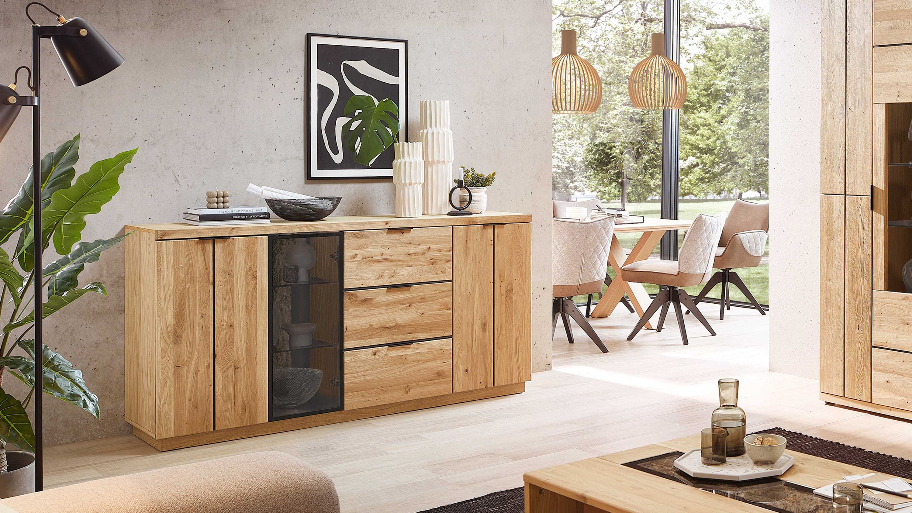 Sideboard aus hellem Holz mit drei Türen drei Schubladen und einer Glastür in modernem Wohnzimmer