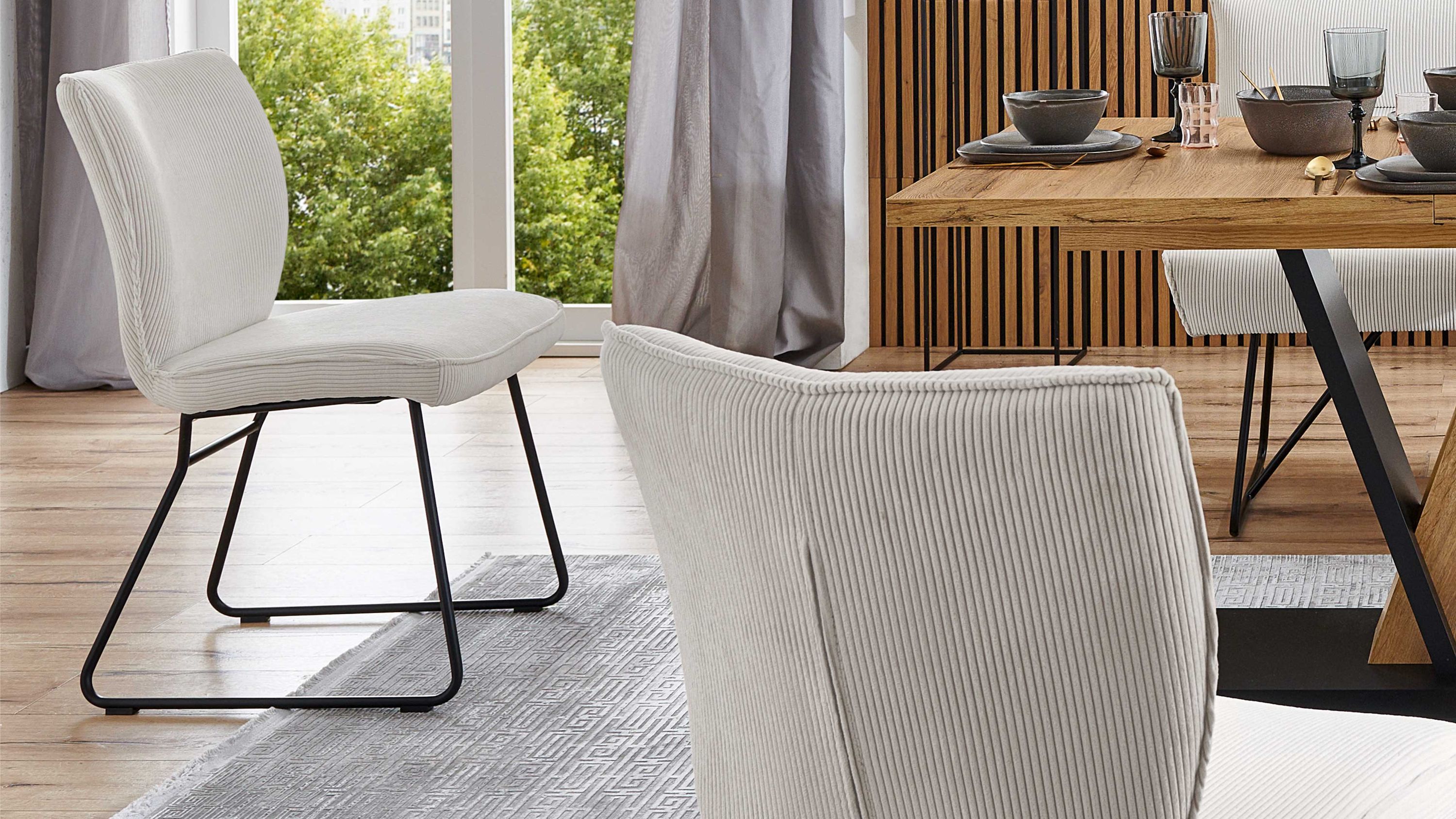 Zwei cremeweiße Polsterstühle mit Cordbezug und schwarzem Metallgestell vor einem Holztisch