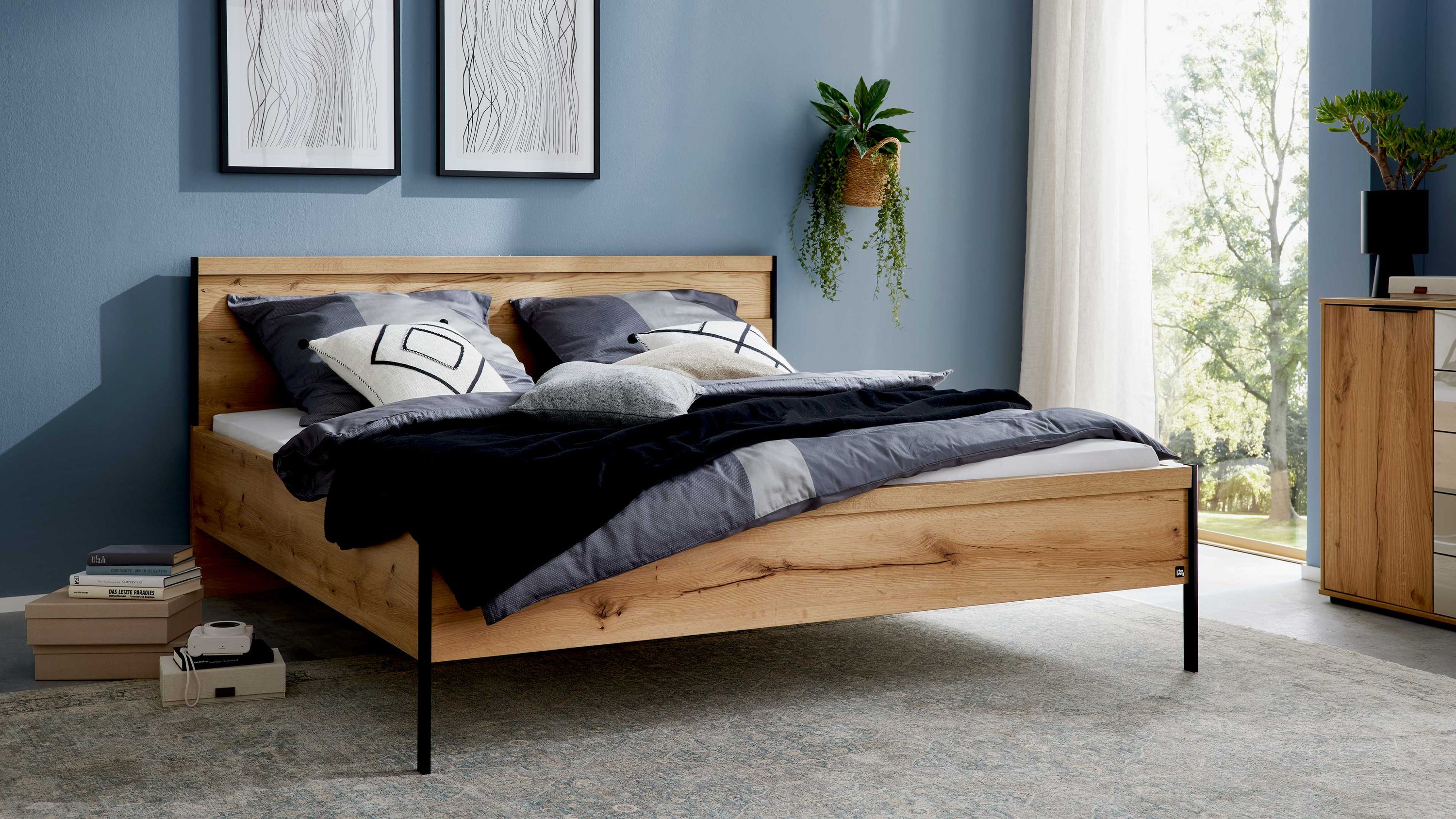 Bettgestell aus Holzoptik mit schwarzem Metallrahmen und Kopfteil in einem Schlafzimmer mit blauen Wänden
