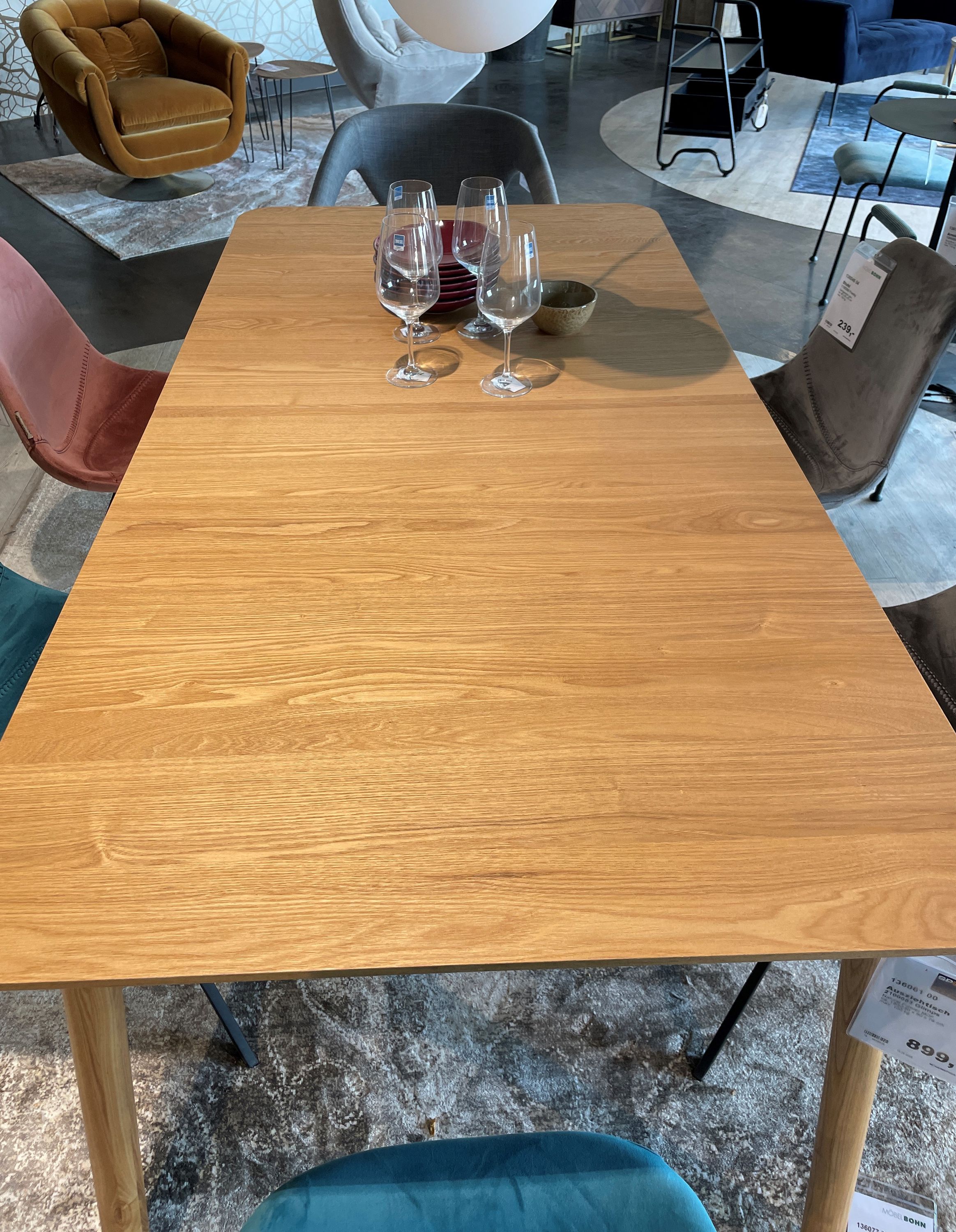 Rechteckiger Holztisch mit glatter Oberfläche, dekoriert mit Weingläsern, kleinen Schalen und umgeben von Samtstühlen in verschiedenen Farben.