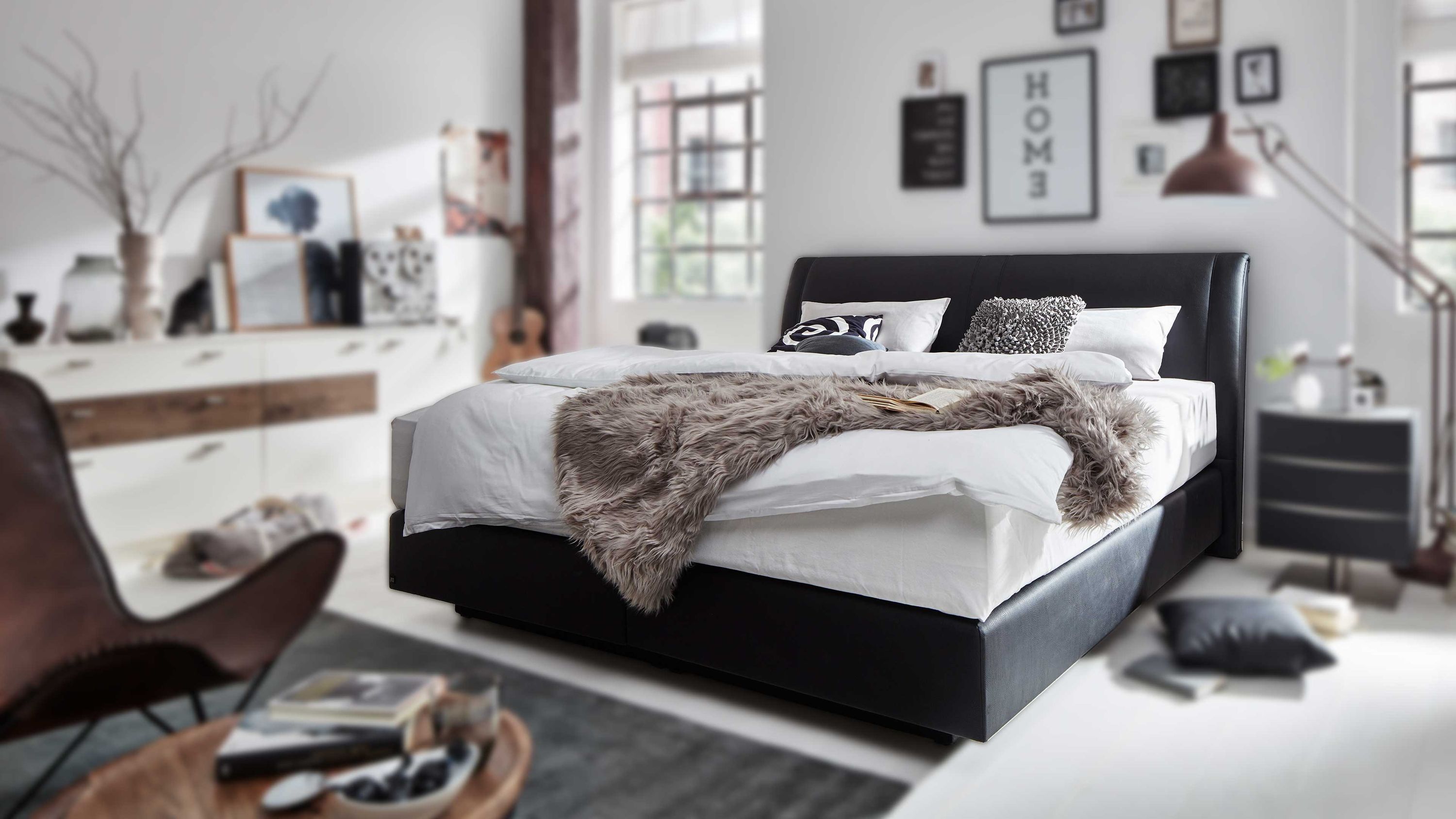 Dunkelgraues Boxspringbett mit gepolstertem Kopfteil und weißer Bettwäsche in modernem Schlafzimmer