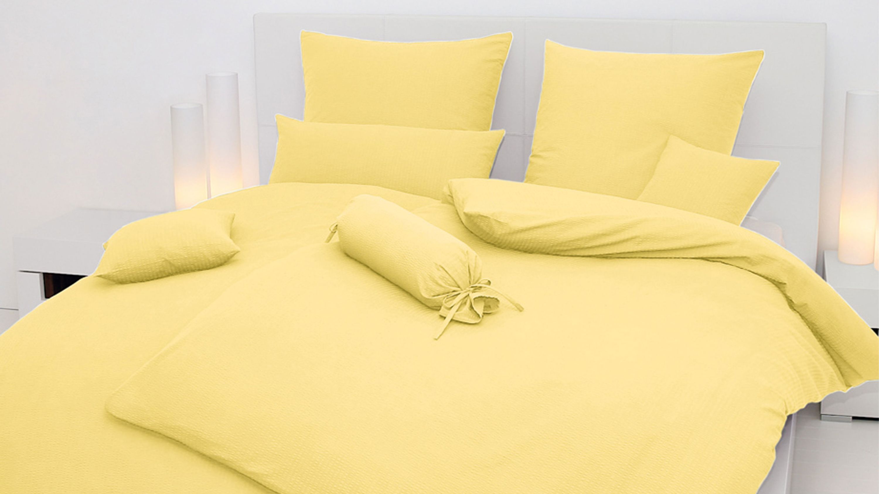 Gelbes Bettwäsche-Set mit Kissen und Zierrolle auf weißem Bett mit Kopfteil