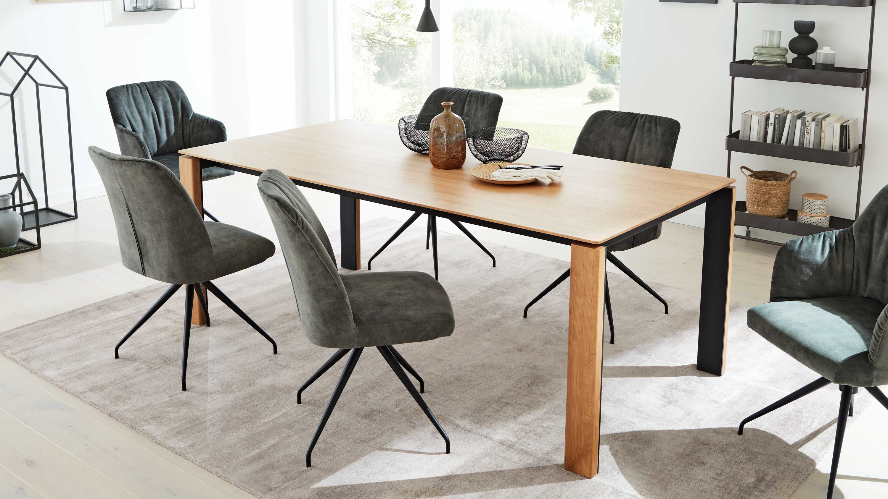 Auszugtisch mit Holzplatte und grauen Stühlen Rechteckiger Esstisch mit Holzplatte und schwarzen Metallbeinen umgeben von sechs grauen Stühlen mit Metallbeinen