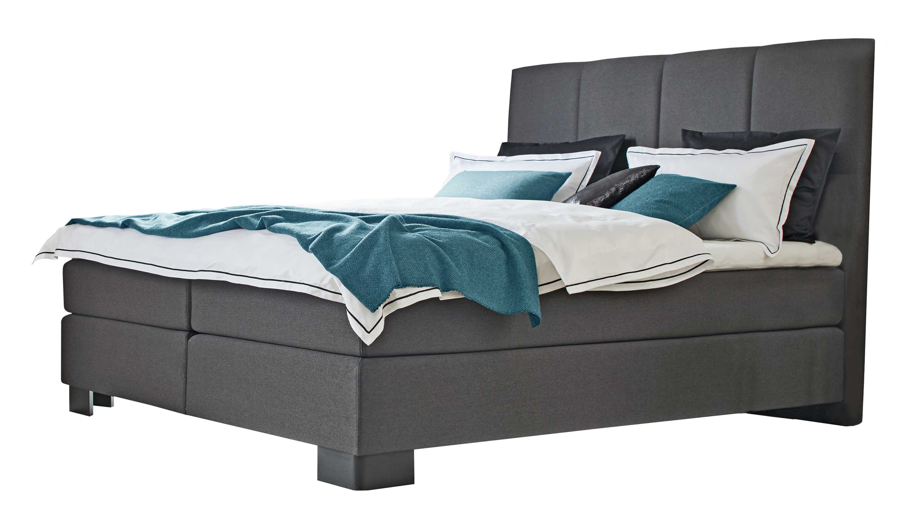 Boxspringbett mit anthrazitfarbenem Bezug und gepolstertem Kopfteil weiße Bettwäsche und blaue Decke