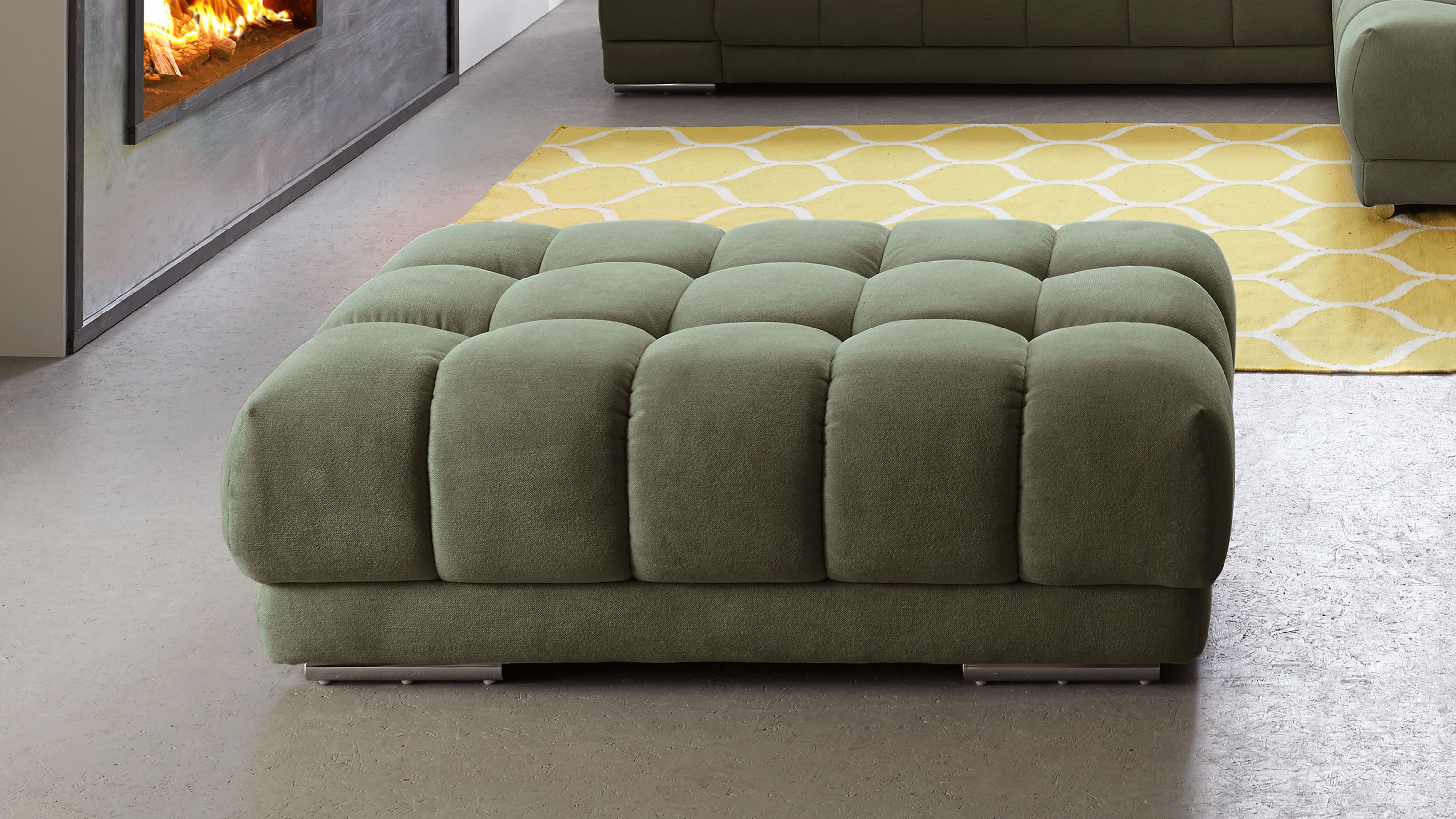 Großer moosgrüner Polsterhocker mit quadratischer Steppung und Metallfüßen vor Sofa und Kamin