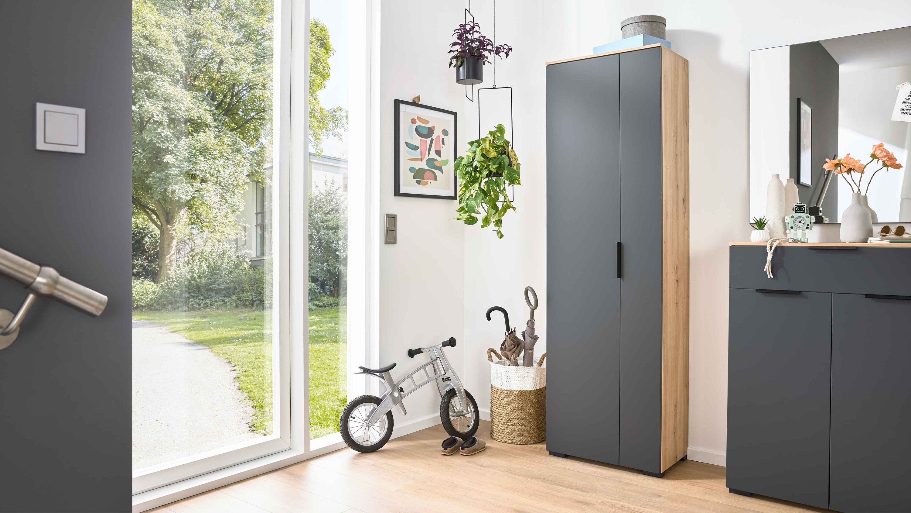 Garderobenschrank mit einer anthrazitfarbenen Tür und seitlichen Holzflächen in heller Farbe in einem hellen Flur