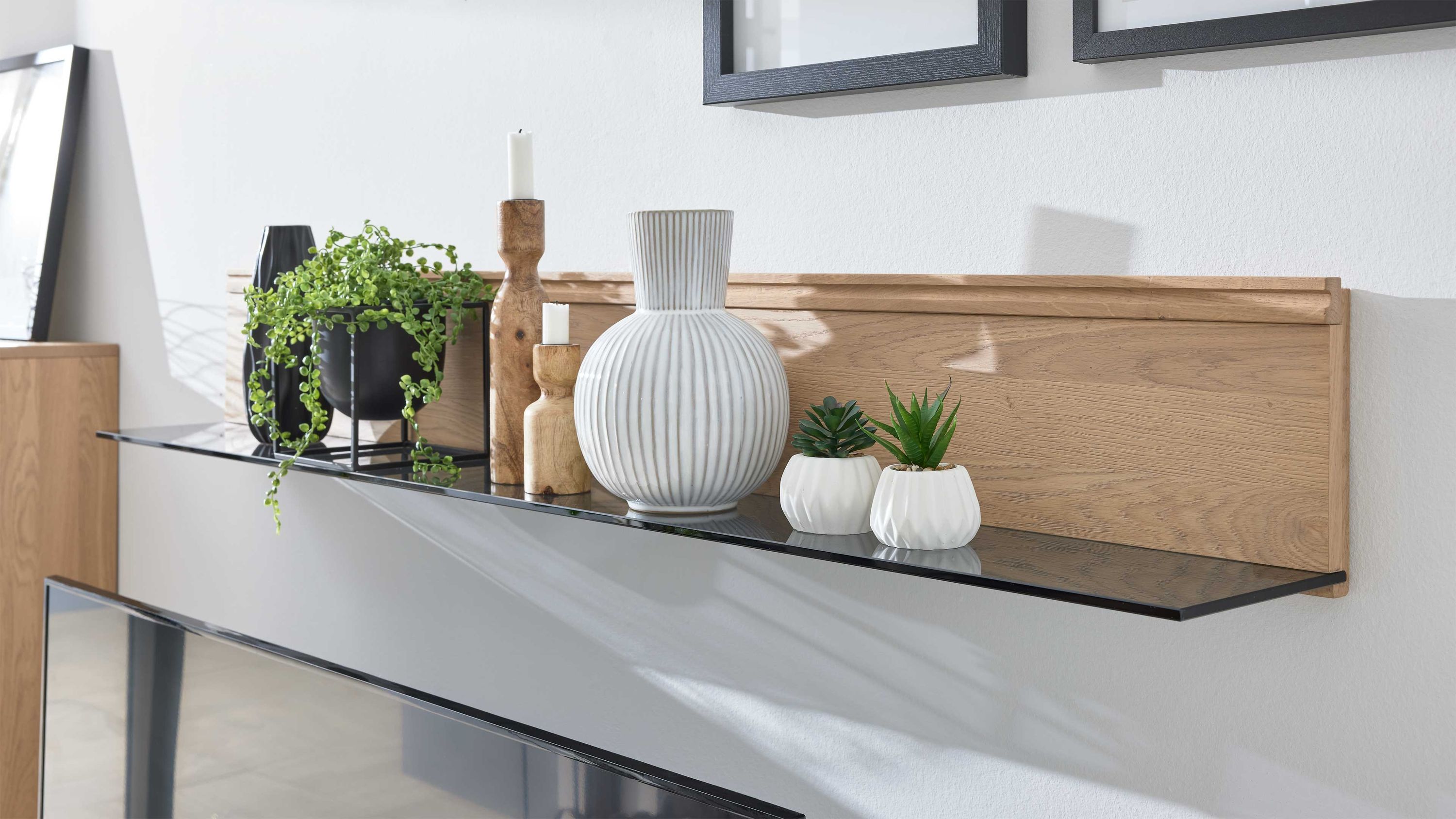 Wandregal mit schwarzer Glasablage und Rückwand aus hellem Holz dekoriert mit Vasen Kerzenhaltern und Pflanzen