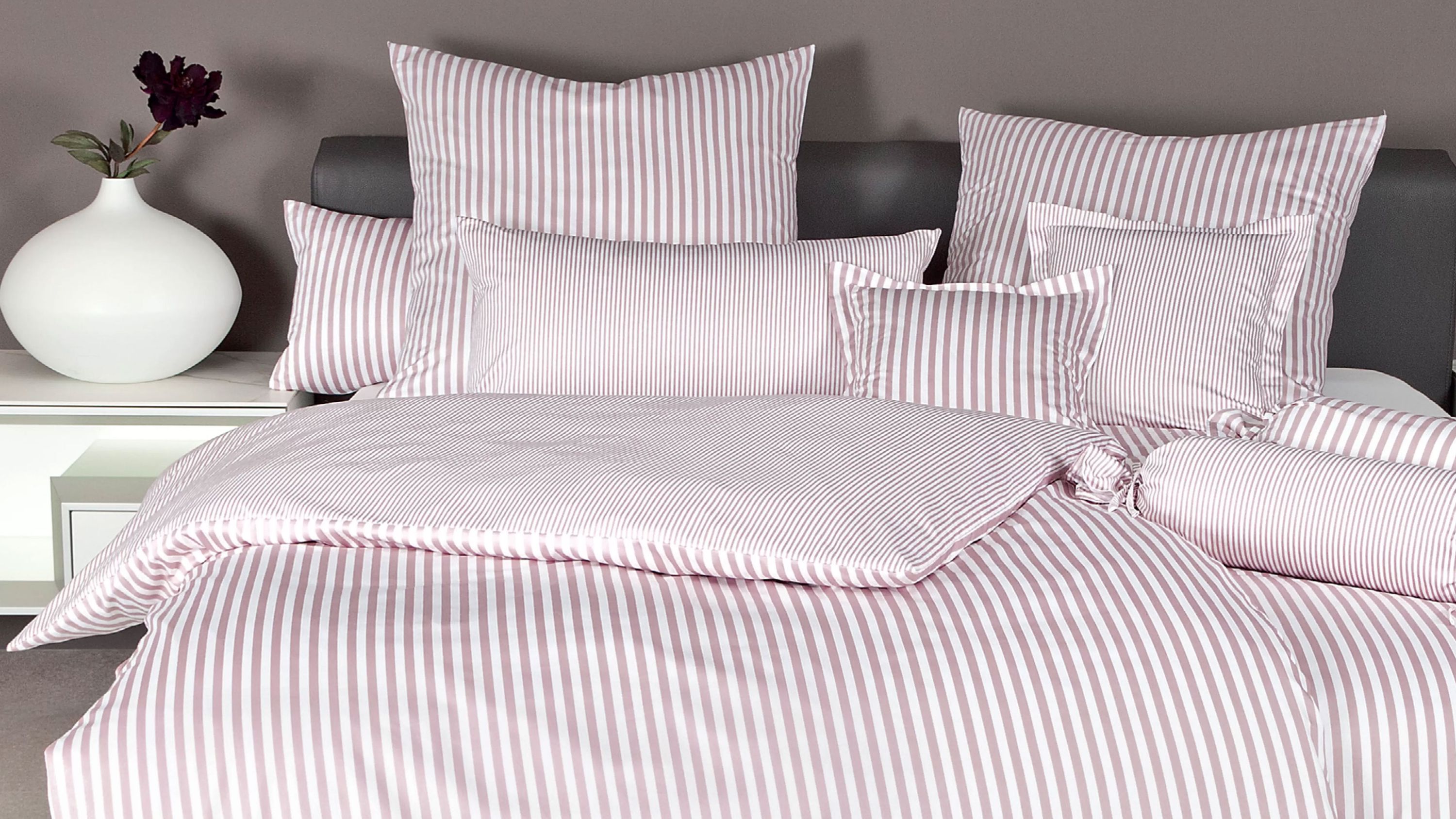 Bettwäsche-Set mit verschiedenen Kissen und Decke in weiß und rot gestreift auf einem Bett mit dunklem Kopfteil
