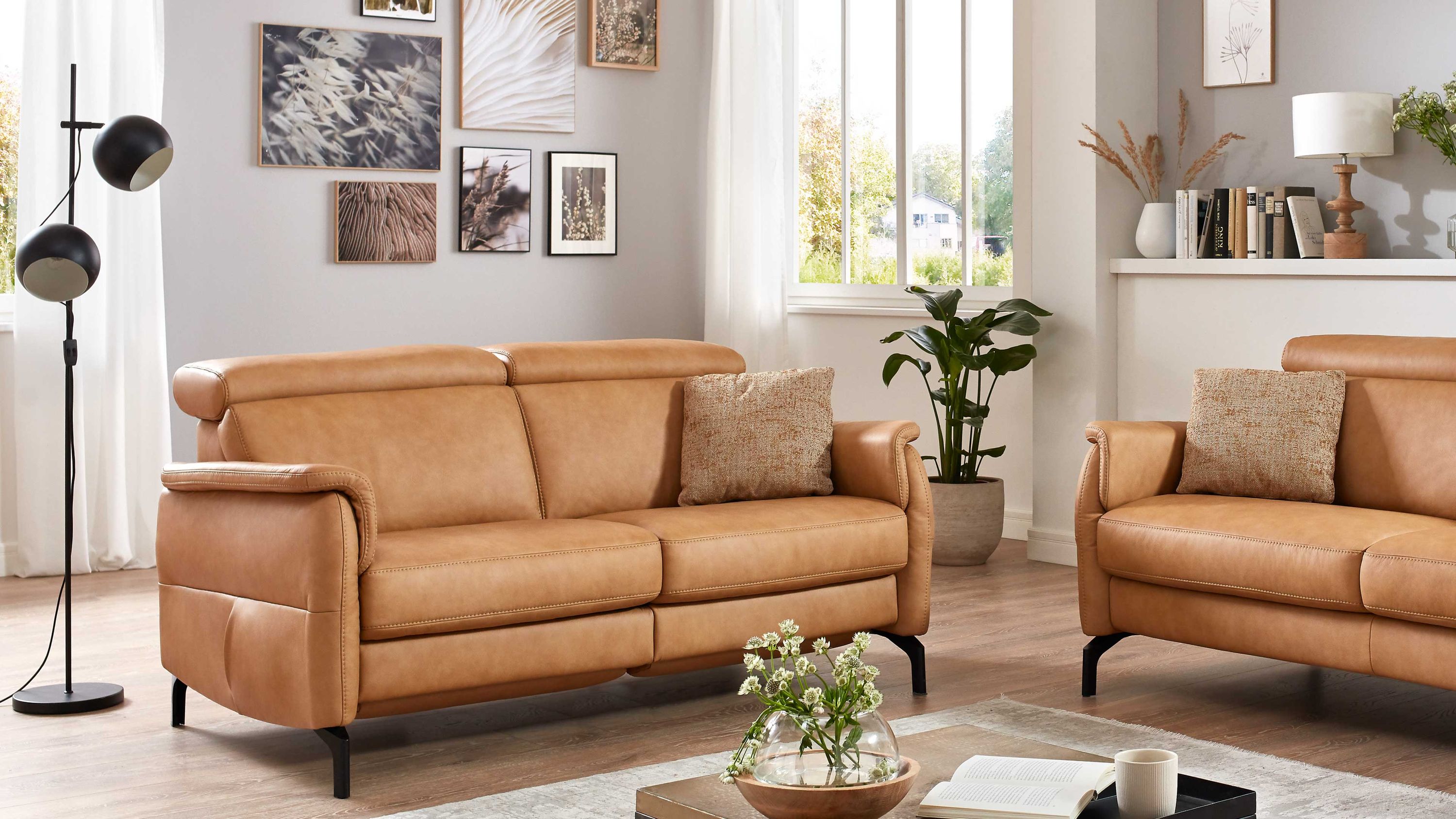 Zweisitziges Sofa mit honigfarbenem Lederbezug Zweisitziges Sofa mit honigfarbenem Lederbezug und zwei Kissen in hellem Wohnzimmer