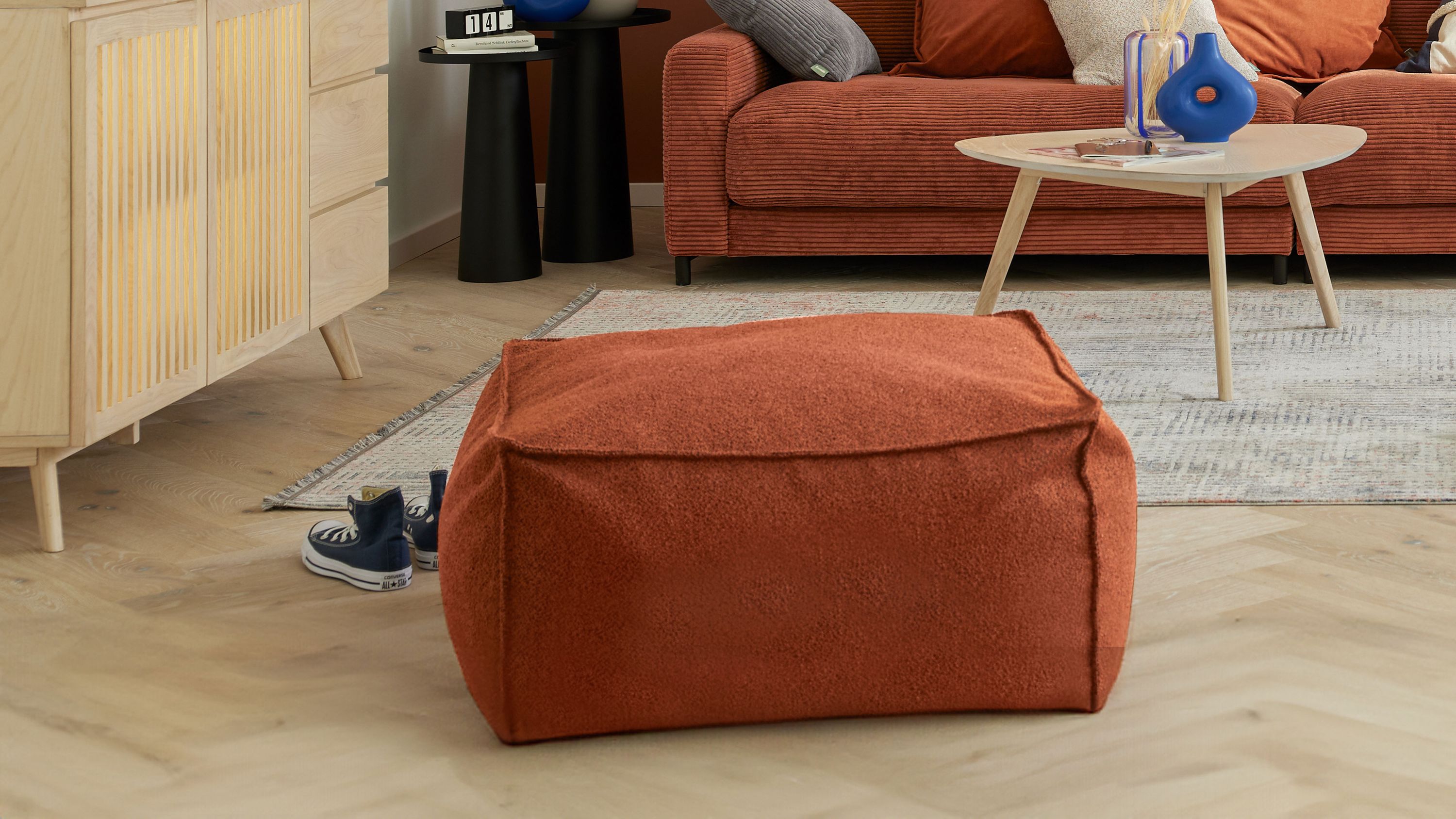 Quadratischer Hocker mit rostfarbenem Stoffbezug in einem Wohnzimmer mit Sofa und Couchtisch