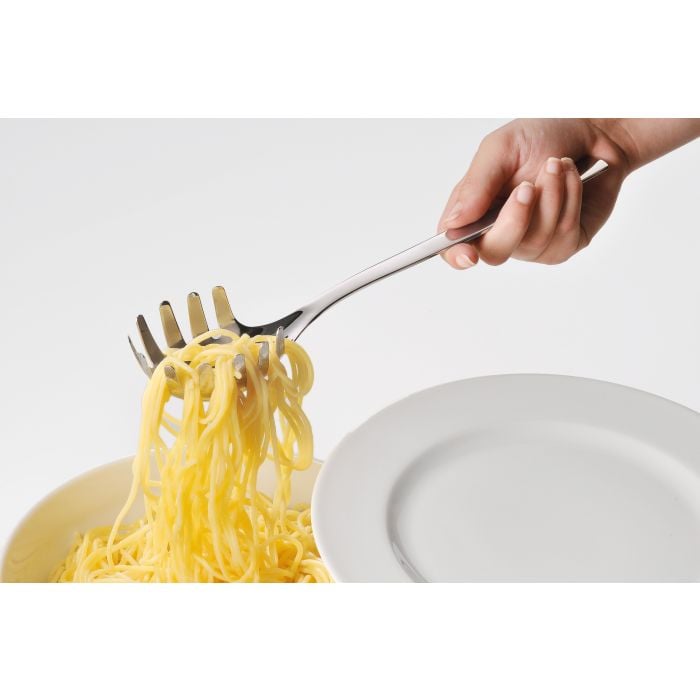 Spaghetti werden serviert auf Teller daneben Seitliche Perspektive: Hand hält Spaghettilöffel mit Nudeln über Schüssel, leerer Teller im Hintergrund