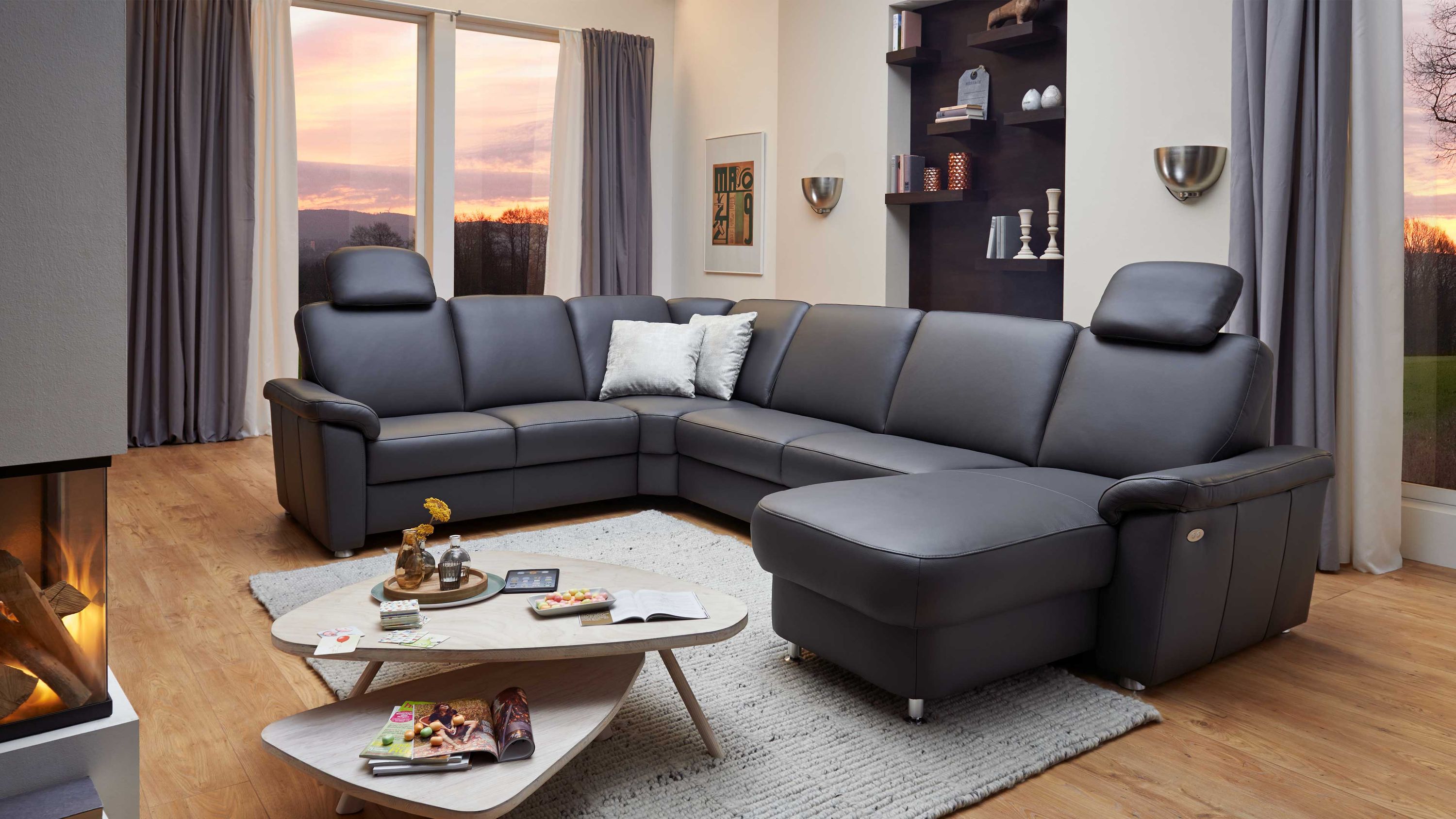 Anthrazitfarbene Wohnlandschaft mit Lederbezug und Metallfüßen in einem Wohnzimmer mit großen Fenstern