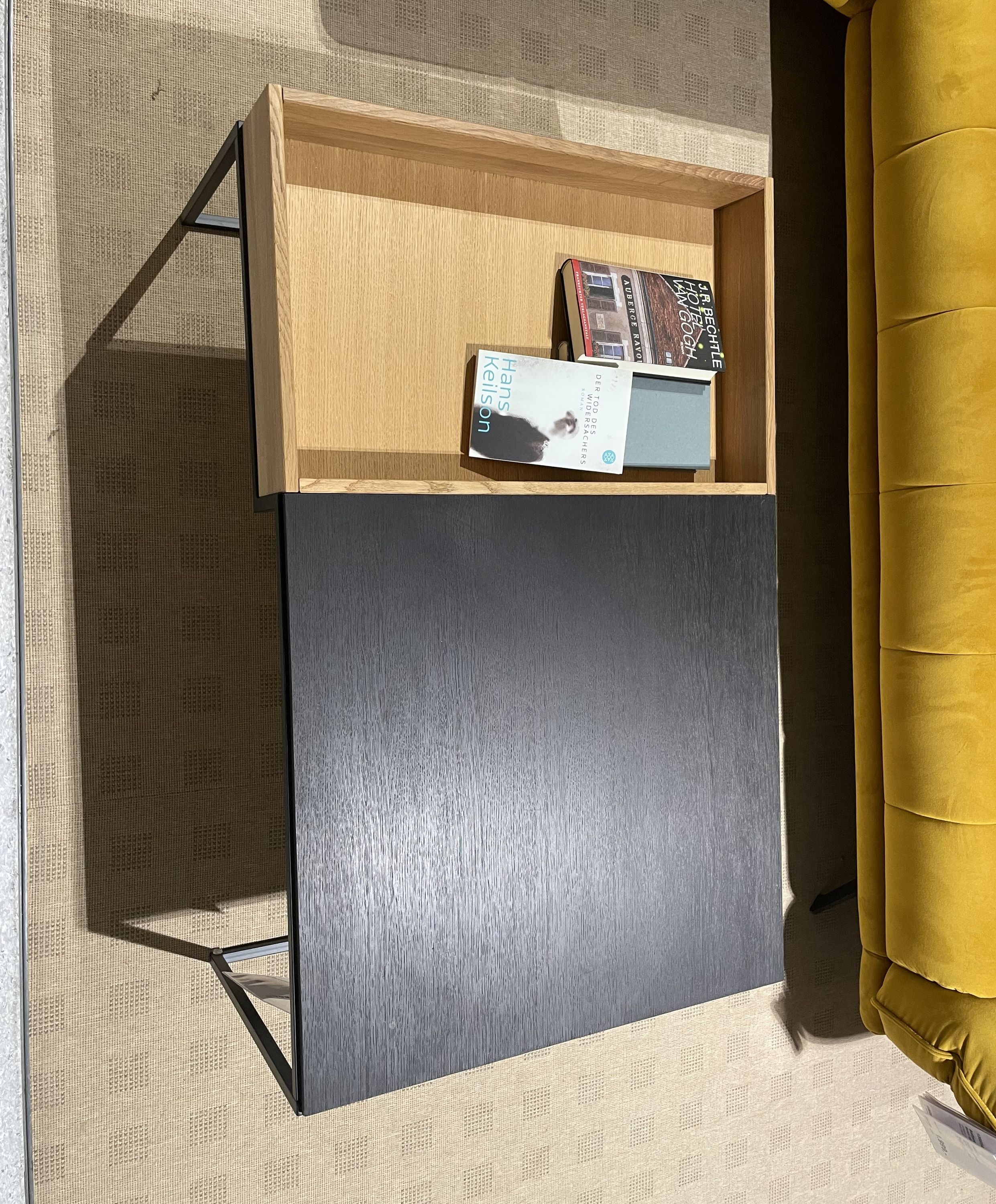 Rechteckiger Couchtisch mit schwarzer Platte und seitlichem offenen Ablagefach aus Holz, bestückt mit Büchern.