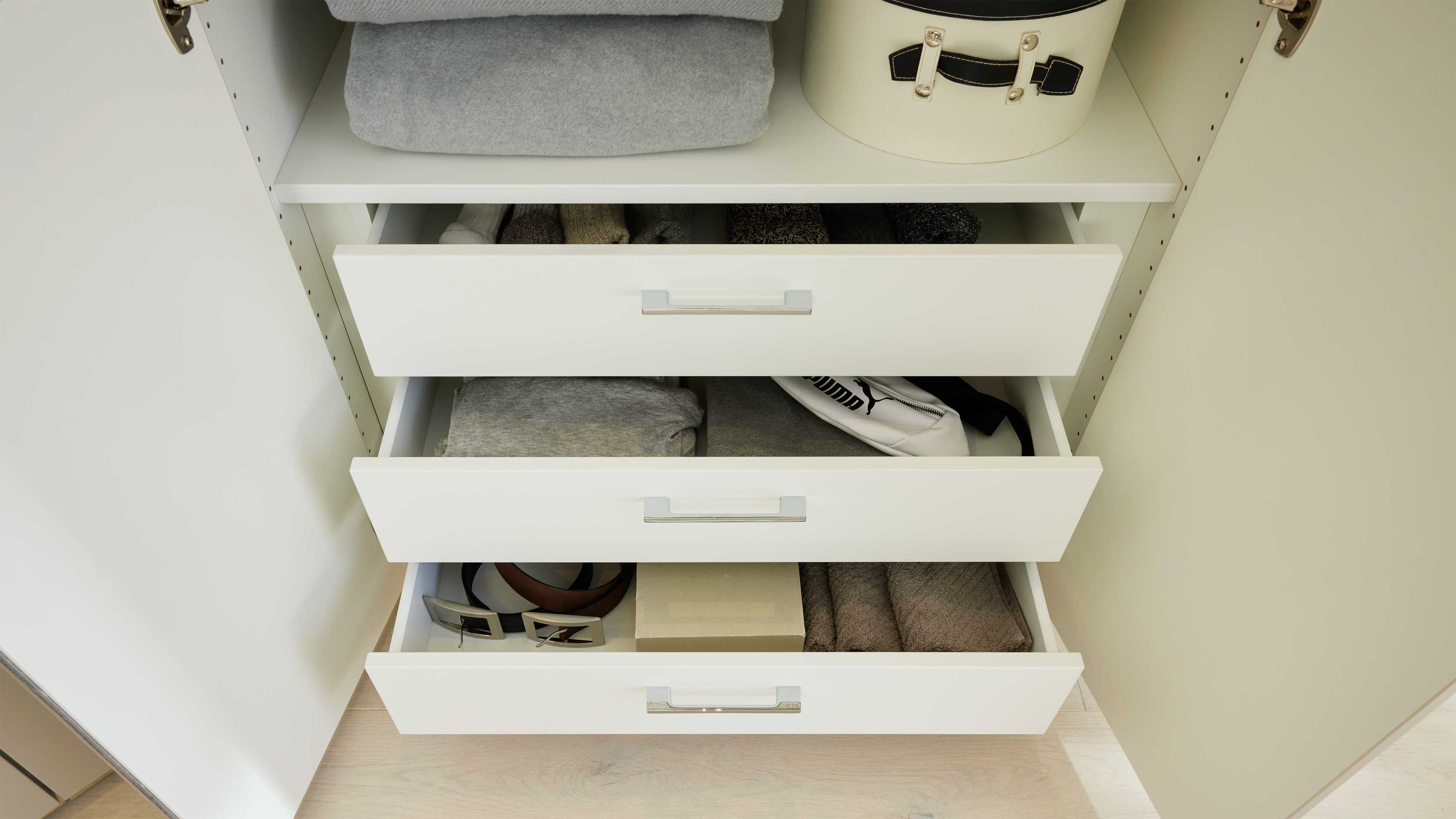 Weißer Kleiderschrank mit drei offenen Innenschubladen und Kleidung darin