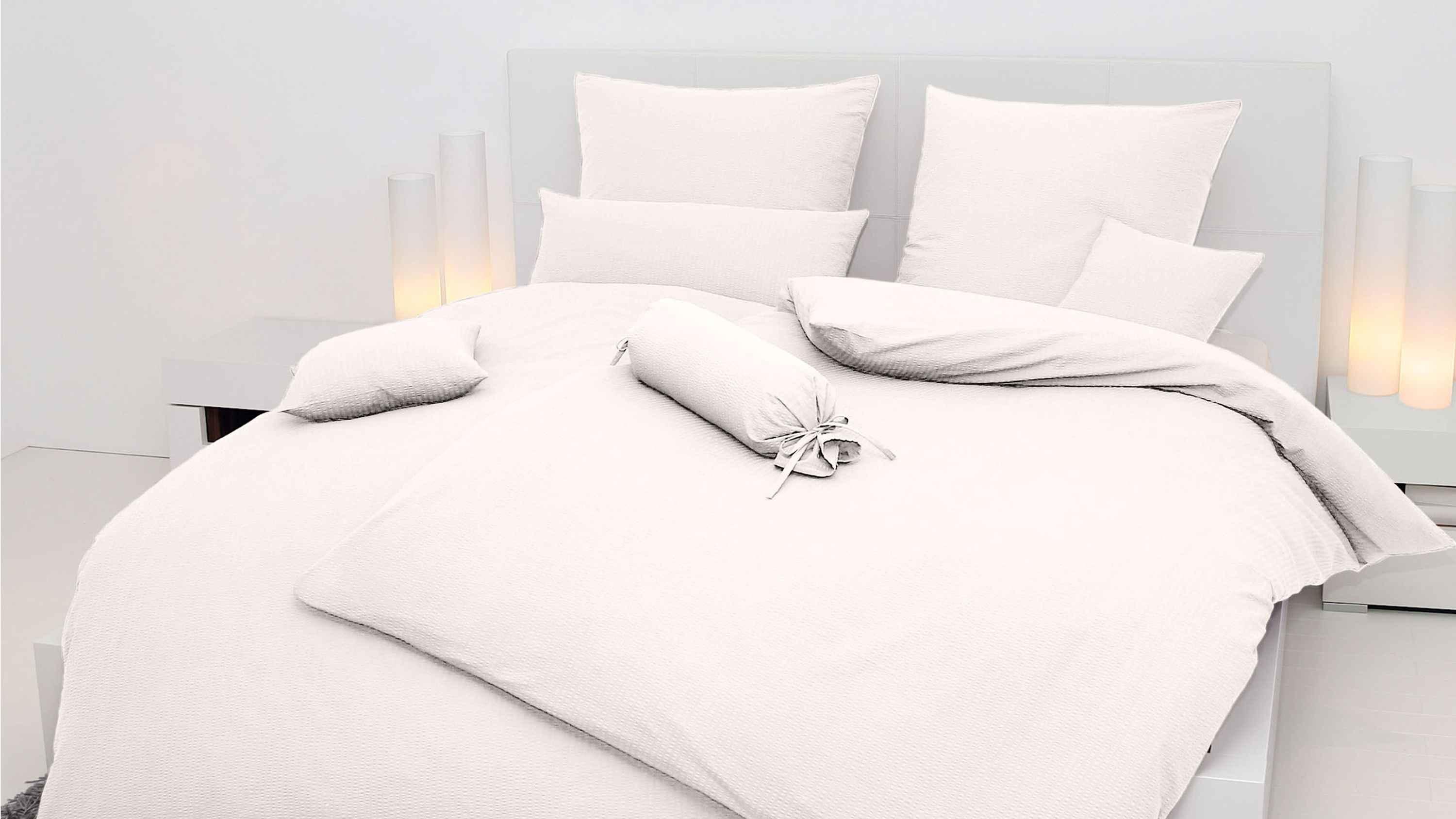 Hellbeige Bettwäsche mit Kissen und Zierkissen auf einem weißen Bett in einem hellen Raum
