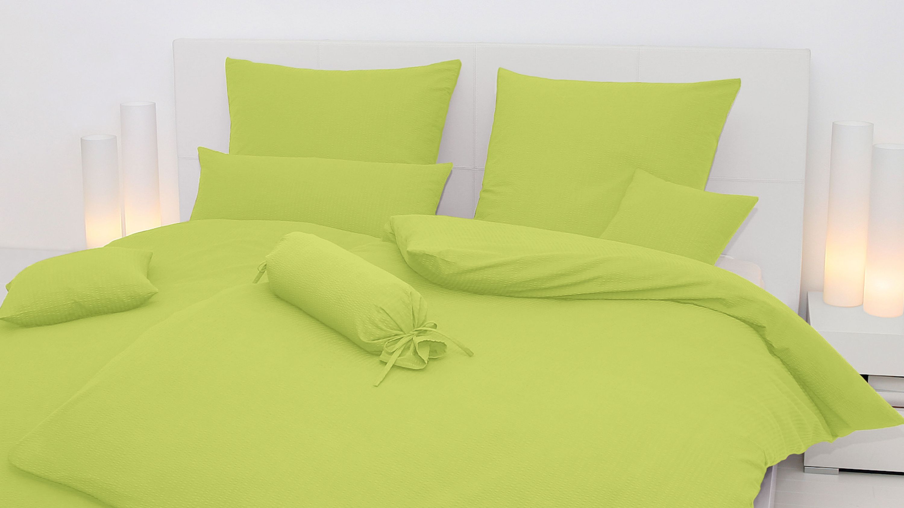 Bett mit apfelgrüner Bettwäsche bestehend aus Kissen Decke und Zierkissen in verschiedenen Formen