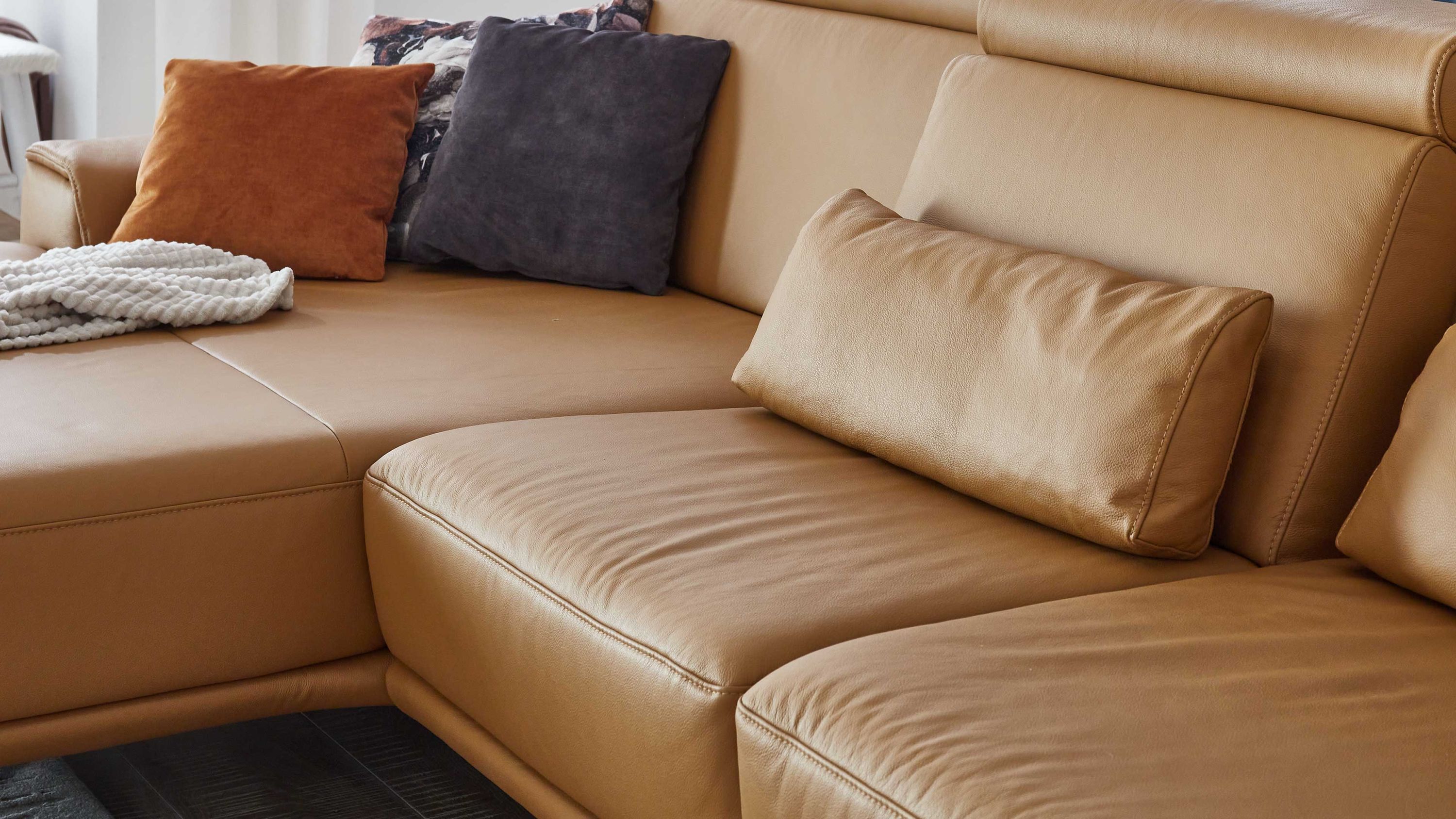 Beige Nierenkissen auf braunem Ledersofa mit weiteren Kissen in Orange und Dunkelgrau