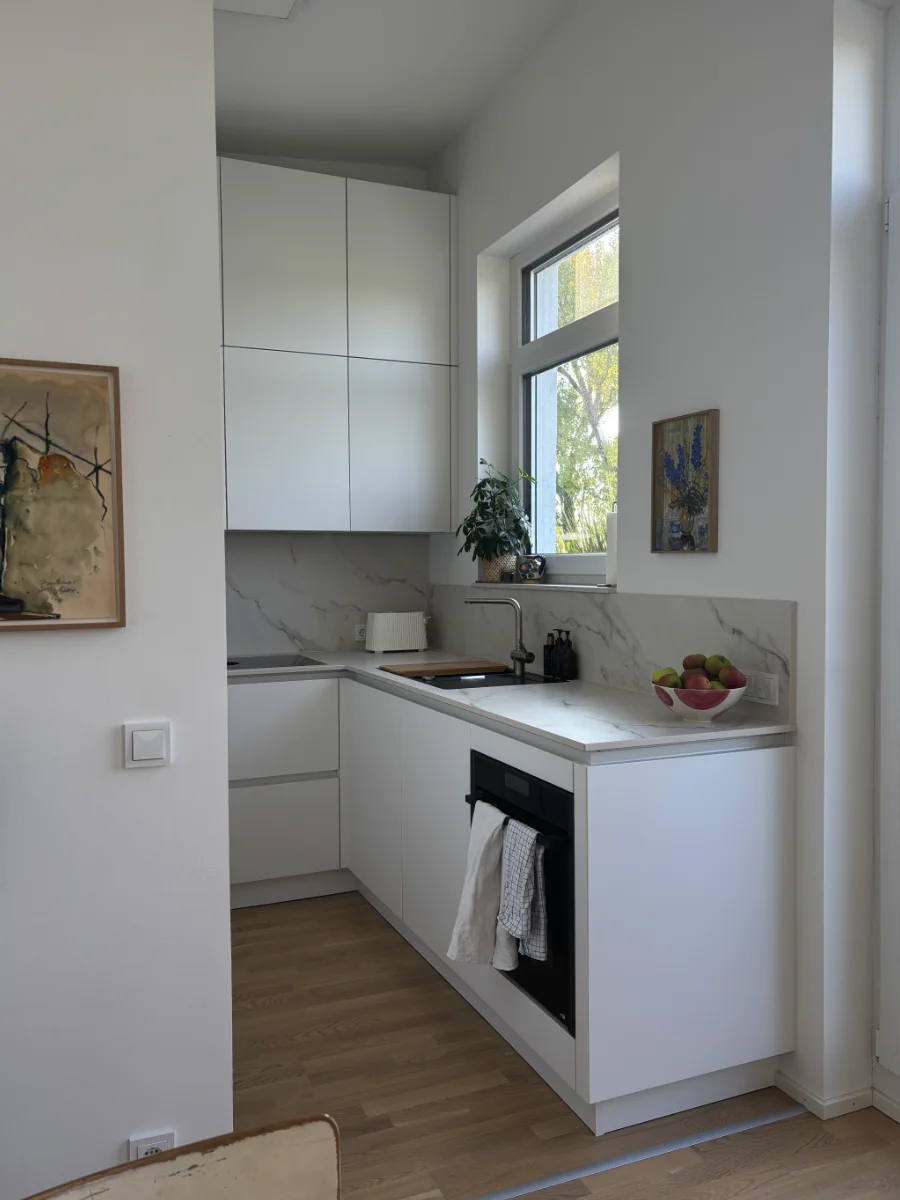 Kompakte weiße Küche mit Hochschränken, Holzarbeitsplatte, Spüle, Backofen und warmer Unterbauleuchtung.