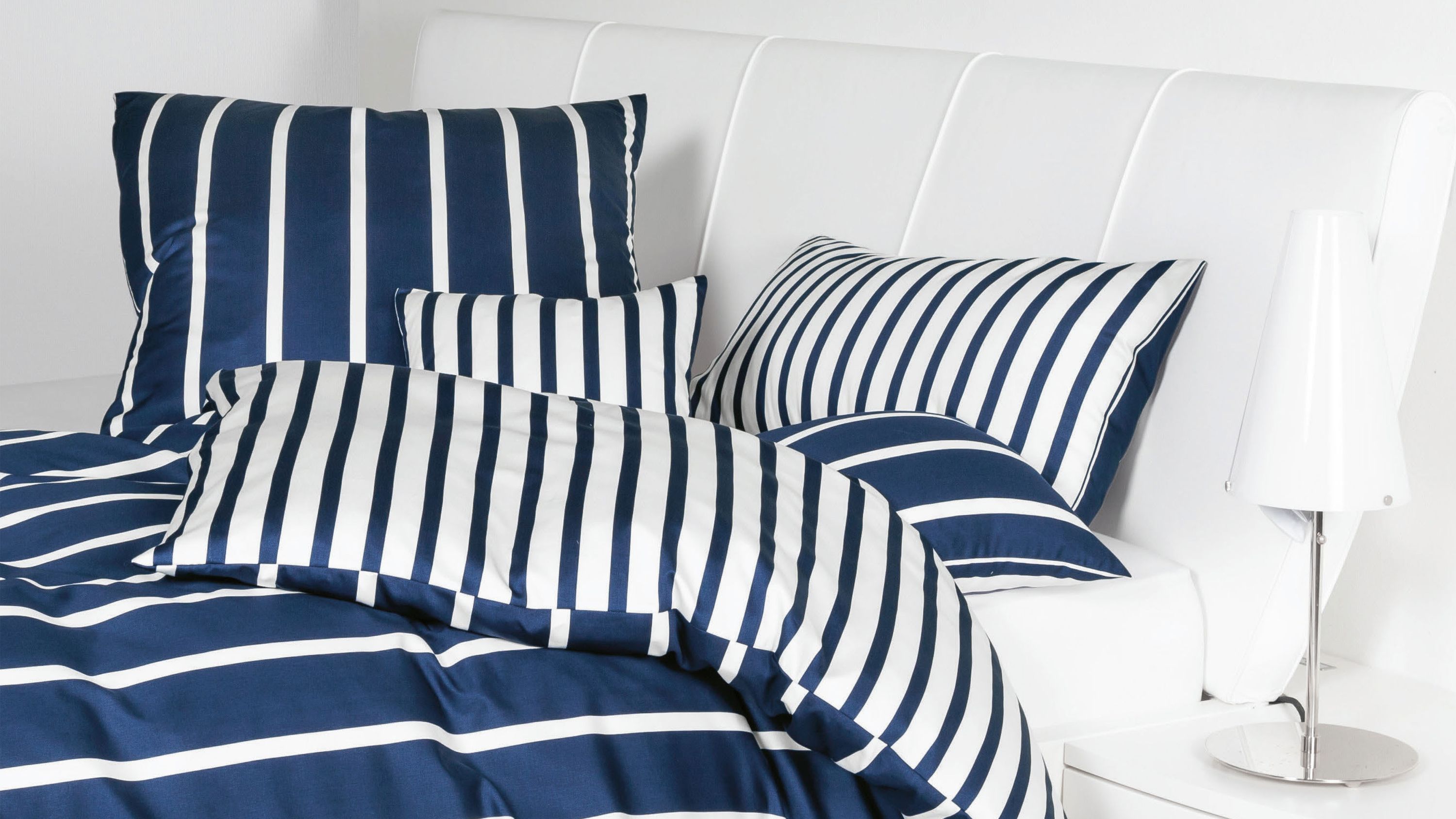 Bettwäsche-Set mit Kissen und Decke in blau und weiß gestreift auf weißem Polsterbett