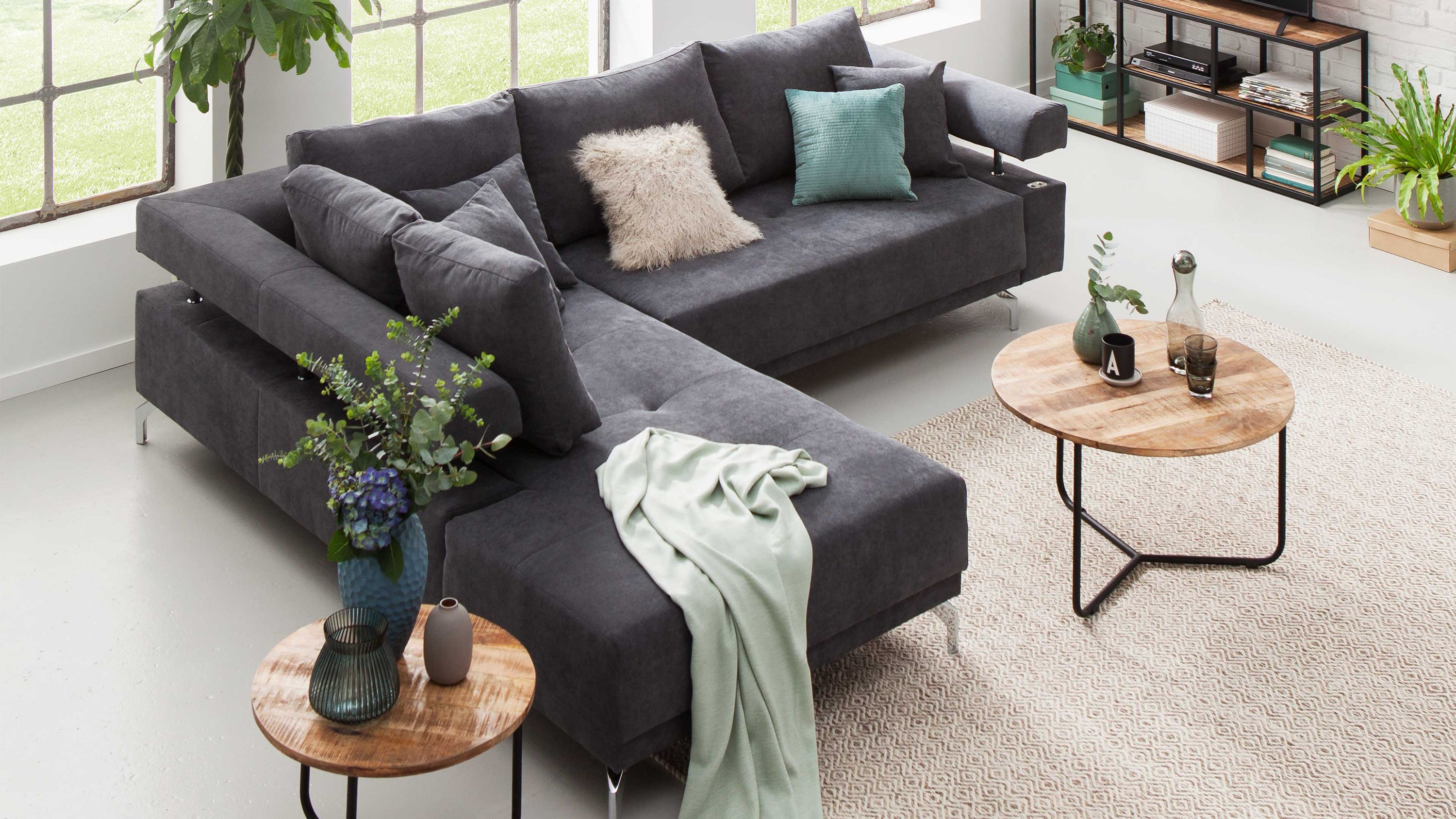 Anthrazitfarbenes Ecksofa mit Metallfüßen und mehreren Kissen in einem hellen Wohnzimmer