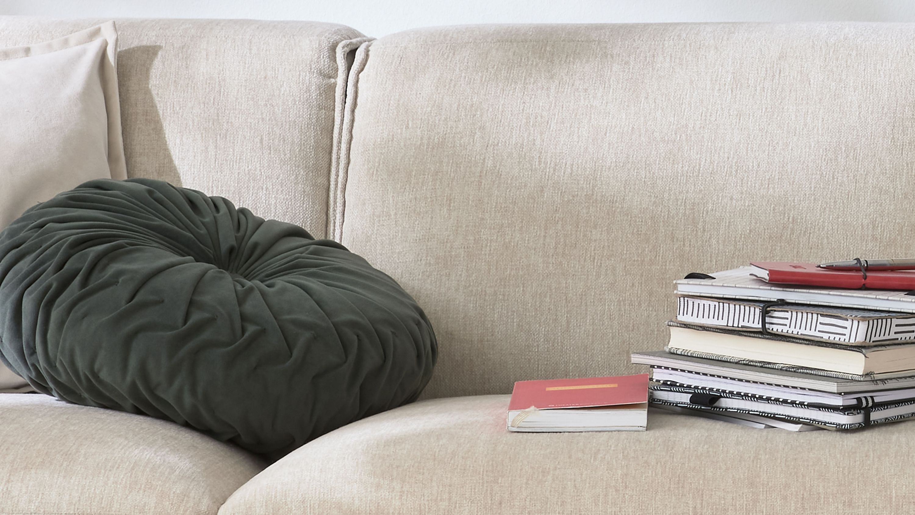 Rundes khakifarbenes Kissen mit Faltenmuster auf einem hellen Sofa