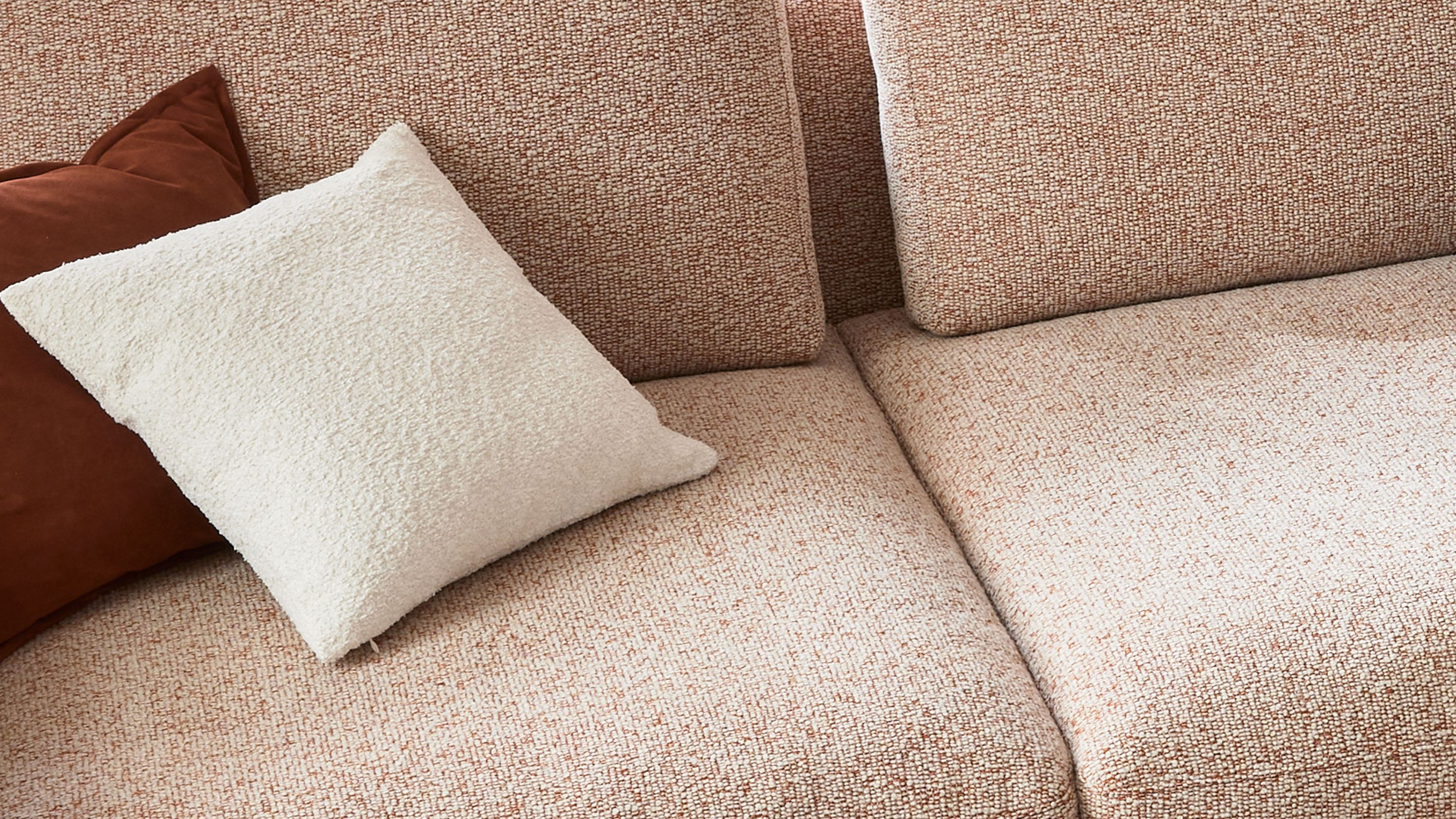 Quadratisches weißes Kissen mit strukturierter Oberfläche auf hellbeigem Sofa mit braunem Kissen