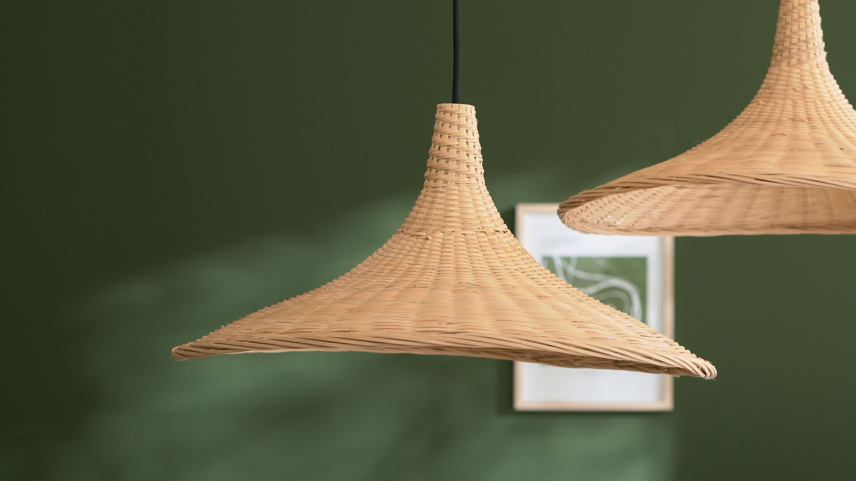 Runde Hängeleuchte aus Bambus mit breiter Krempe Hängende runde Lampe mit breiter Krempe aus geflochtenem Bambus vor grünem Hintergrund
