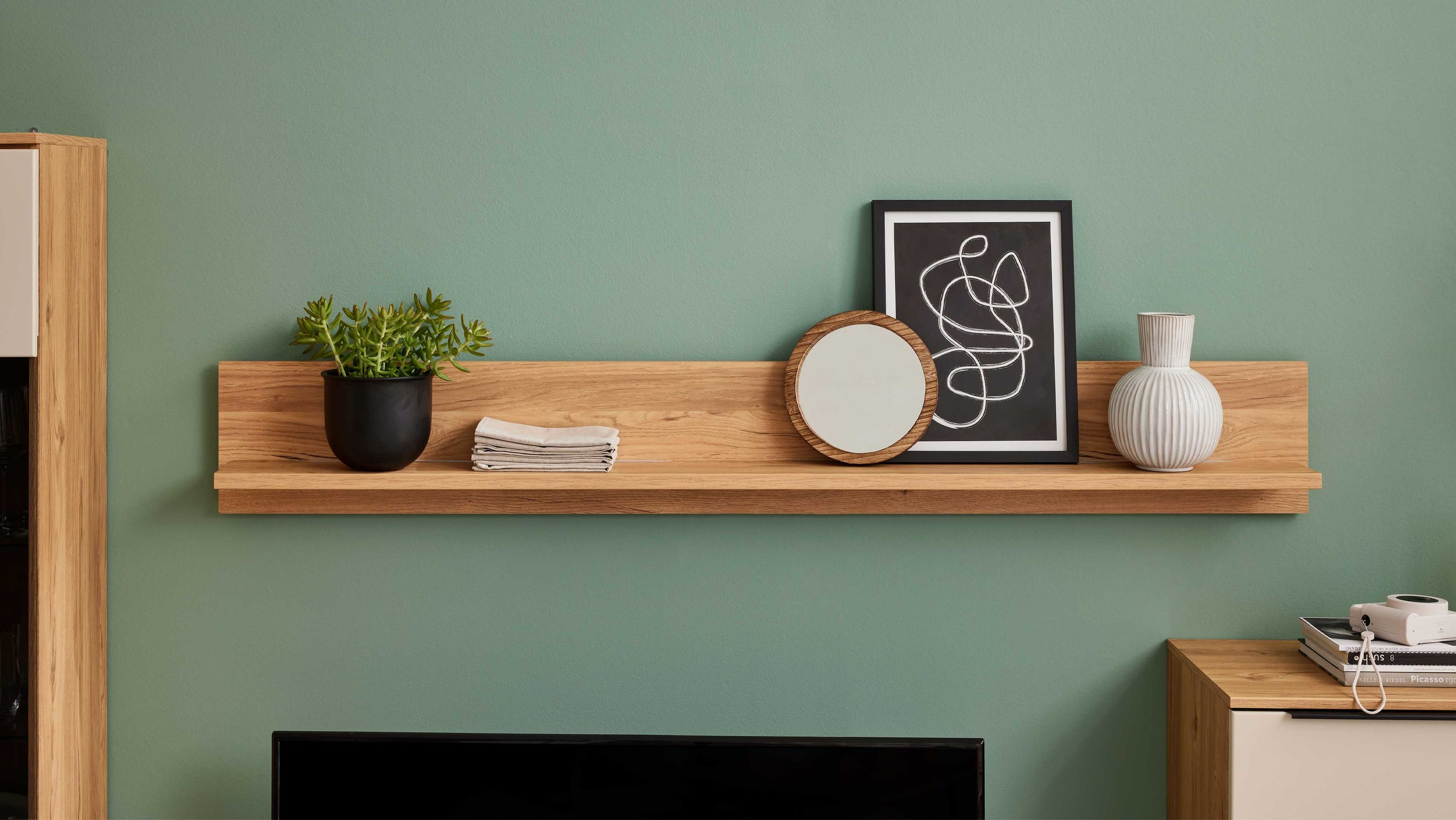 Wandboard in Holzoptik mit Dekoration Rechteckiges Wandboard in Holzoptik mit Pflanzenkübel gefalteten Tüchern rundem Spiegel und Vase an grüner Wand