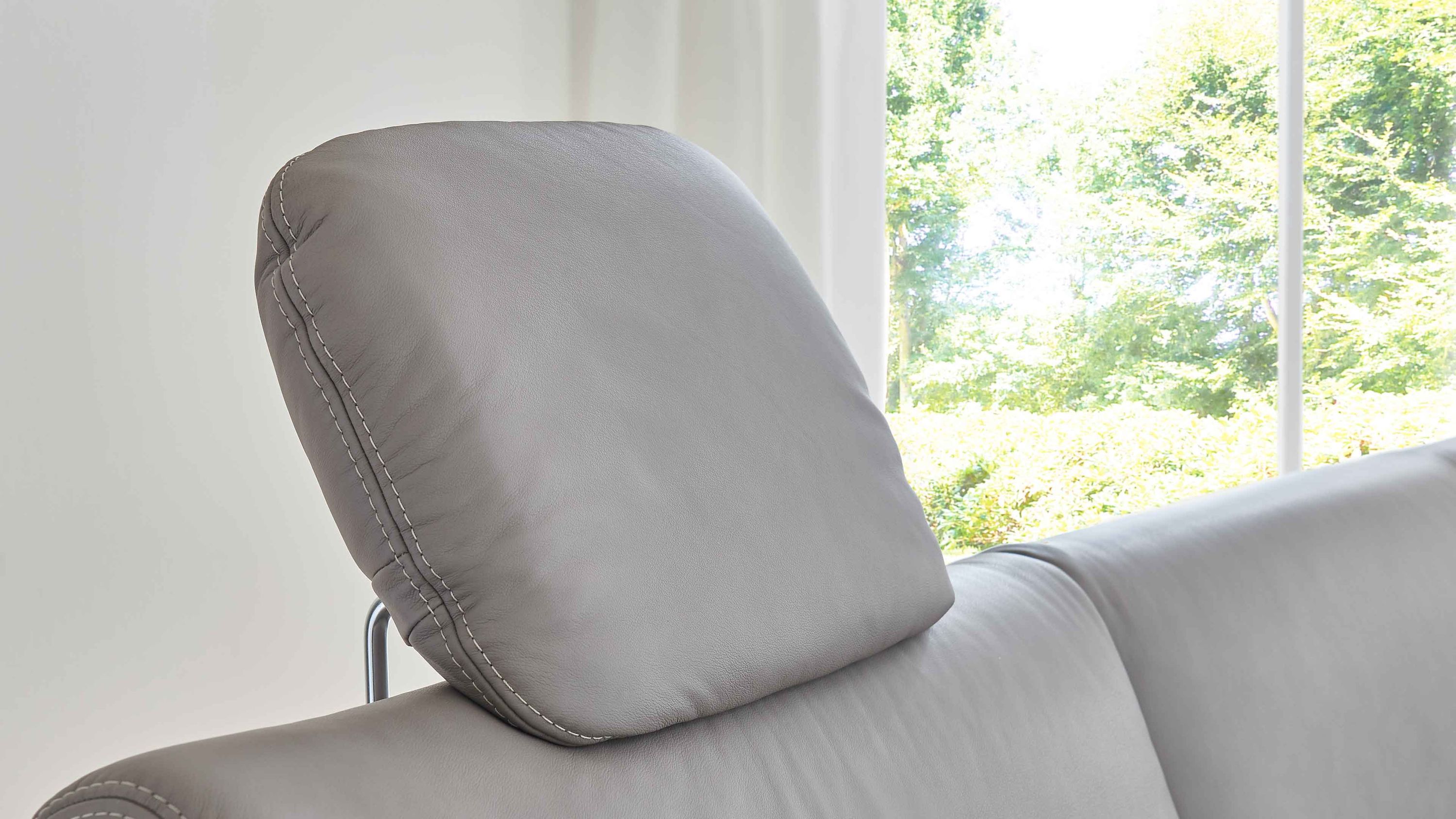 Kopfstütze in grauem Leder mit sichtbaren Nähten auf einem Sofa vor Fenster mit Blick ins Grüne