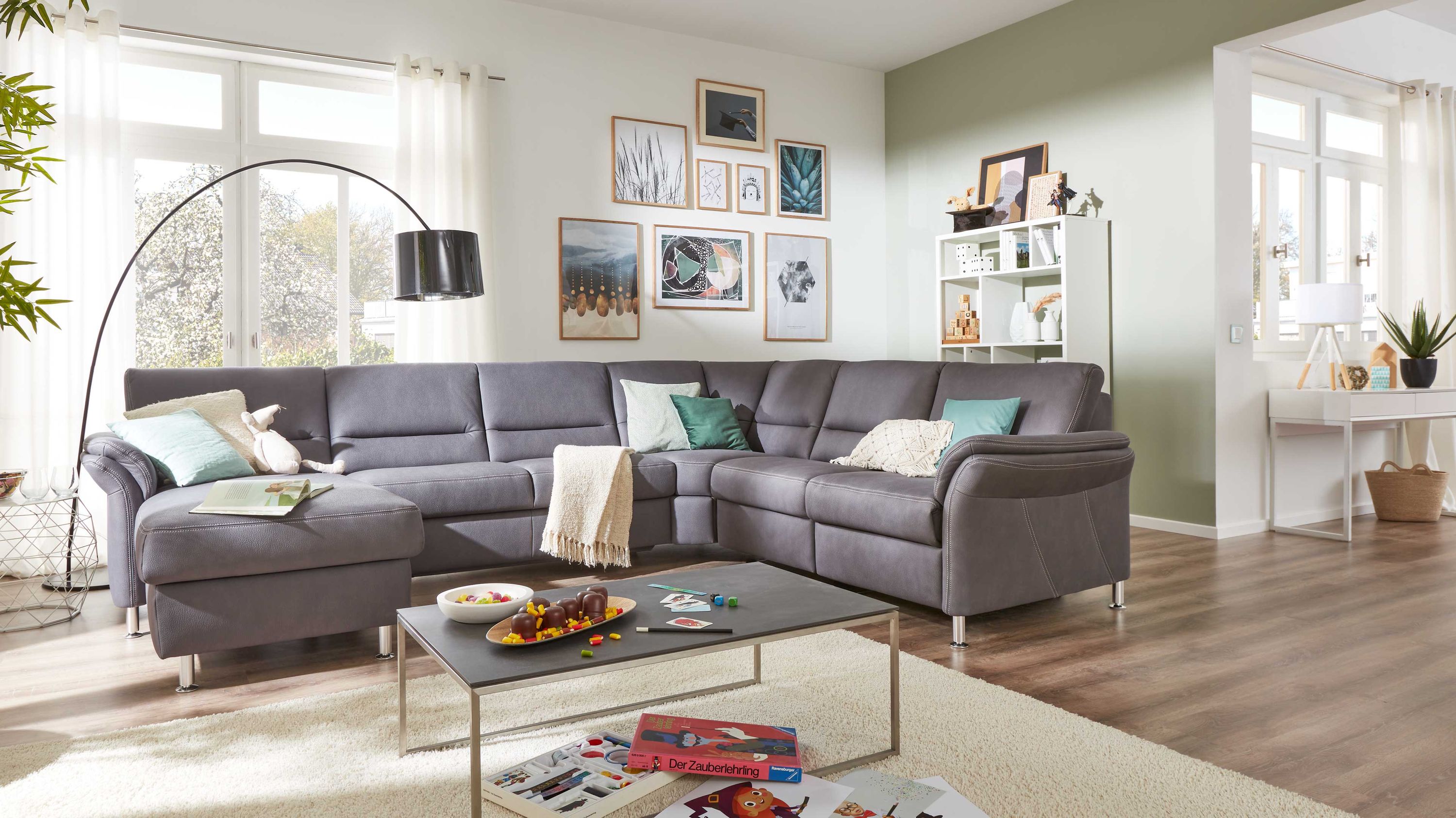 Graue Wohnlandschaft mit Metallfüßen Große graue Wohnlandschaft mit Metallfüßen in hellem Wohnzimmer mit Teppich und Couchtisch