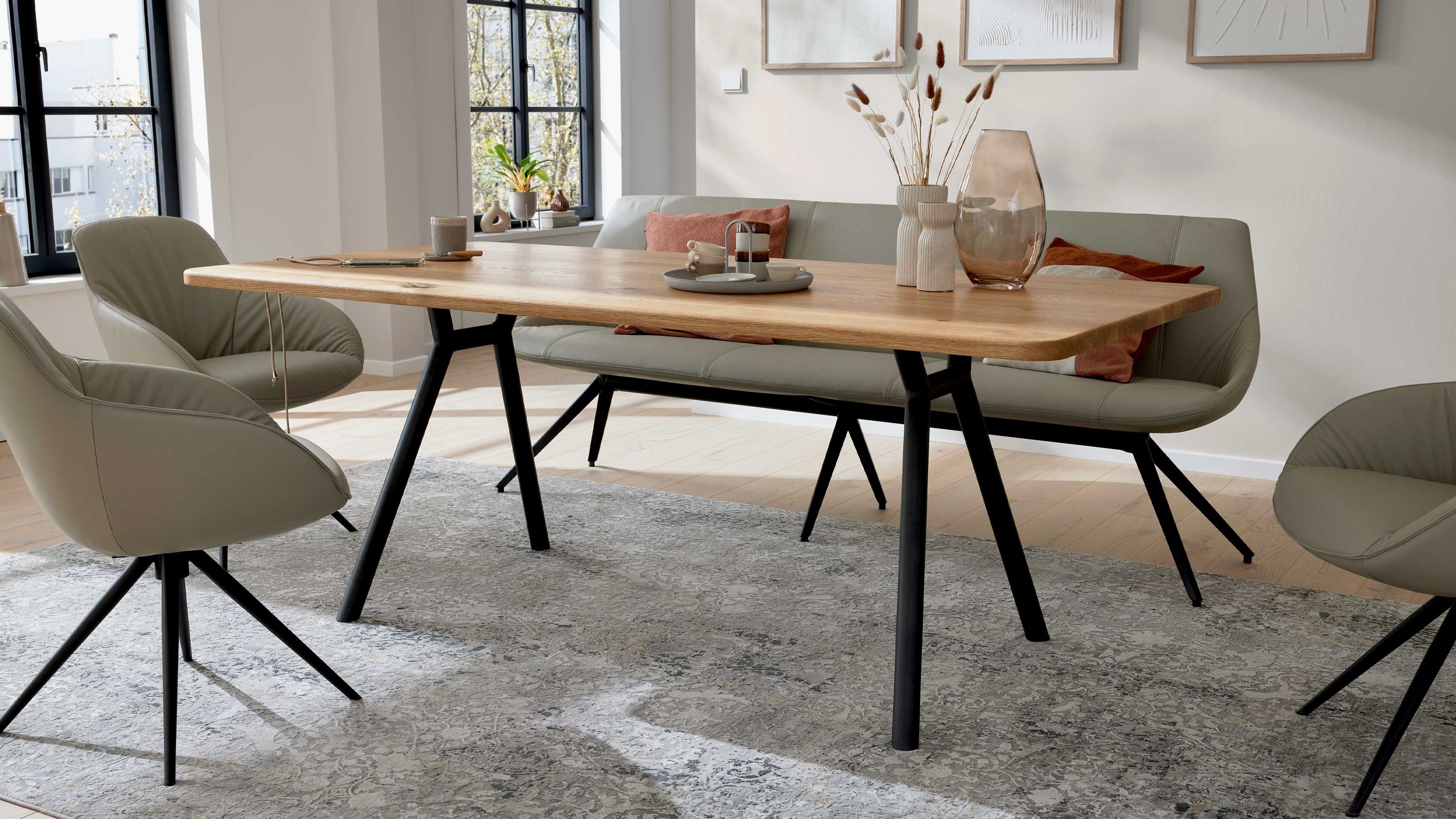 Esstisch mit astiger Holzplatte und schwarzen Metallbeinen in modernem Esszimmer mit grauen Stühlen und Bank