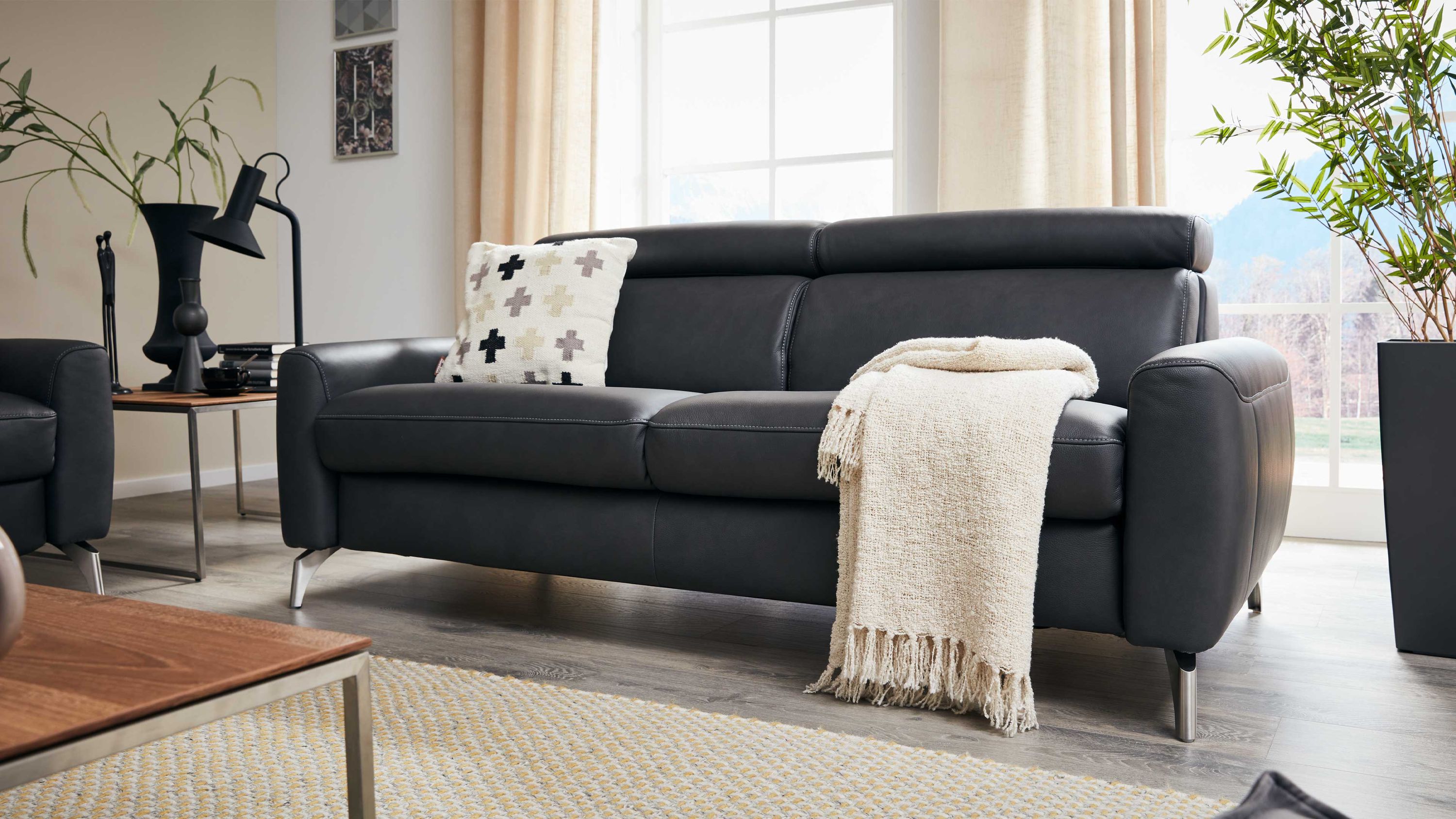 Zweisitziges Sofa mit Bettfunktion in dunklem Leder mit Metallfüßen und zwei Kissen