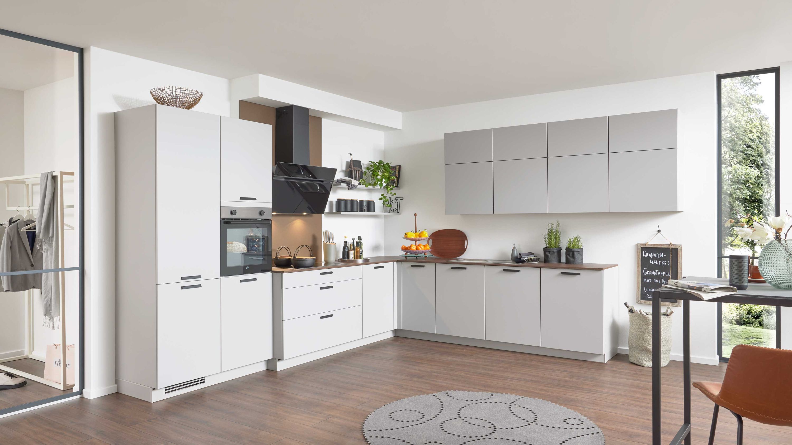 Küche mit weißen und grauen Fronten Holzboden und heller Essecke Küche mit weißen und grauen Schränken Holzboden Einbauofen Esstisch Tageslicht durch große Fenster